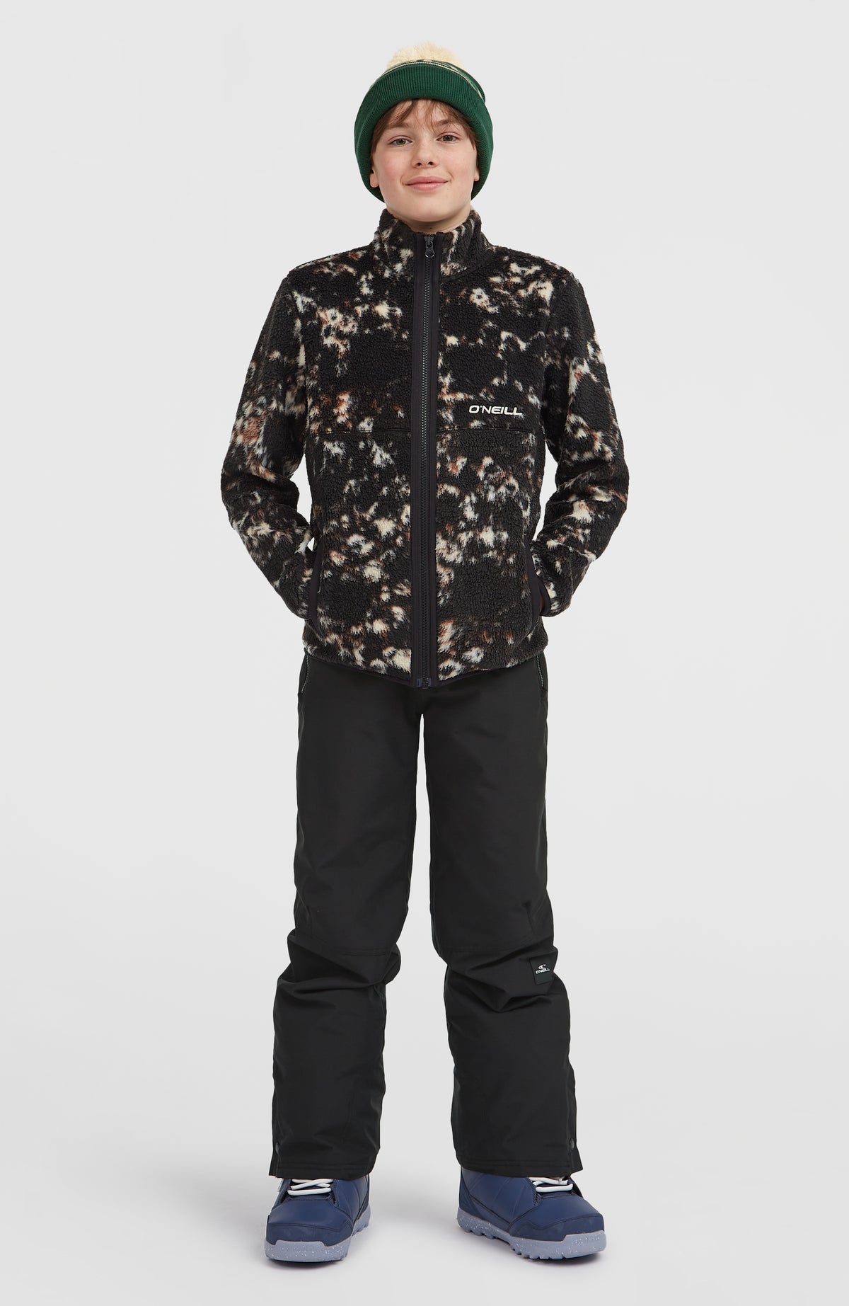 Flauschige Fleecejacke für Jungen, schwarz mit Allover-Muster in Beige, Ganzkörperansicht am Model mit Seitentaschen