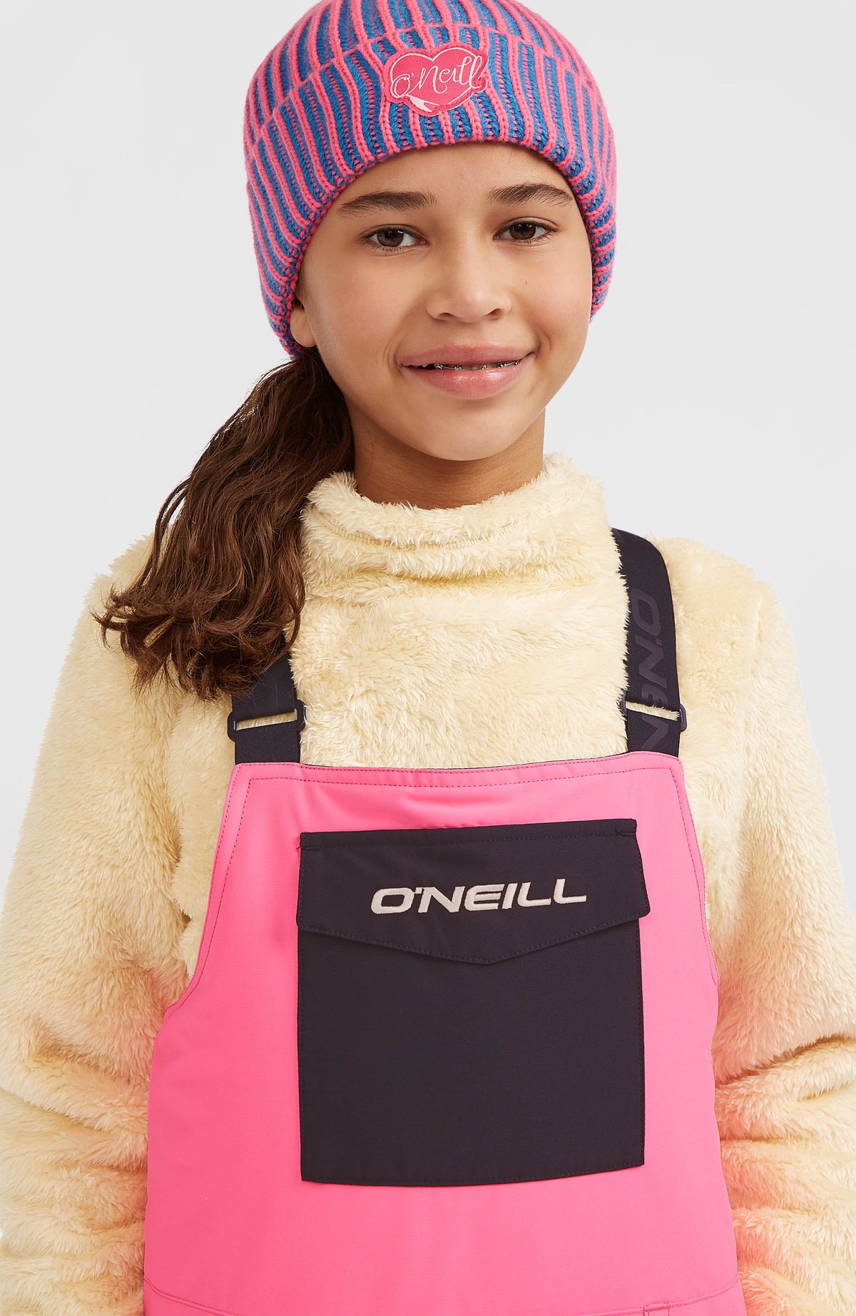 Nahaufnahme des oberen Latzes der pinken FWC'Cruz Bib Skihose am Model, mit dunkler Fronttasche und Logo