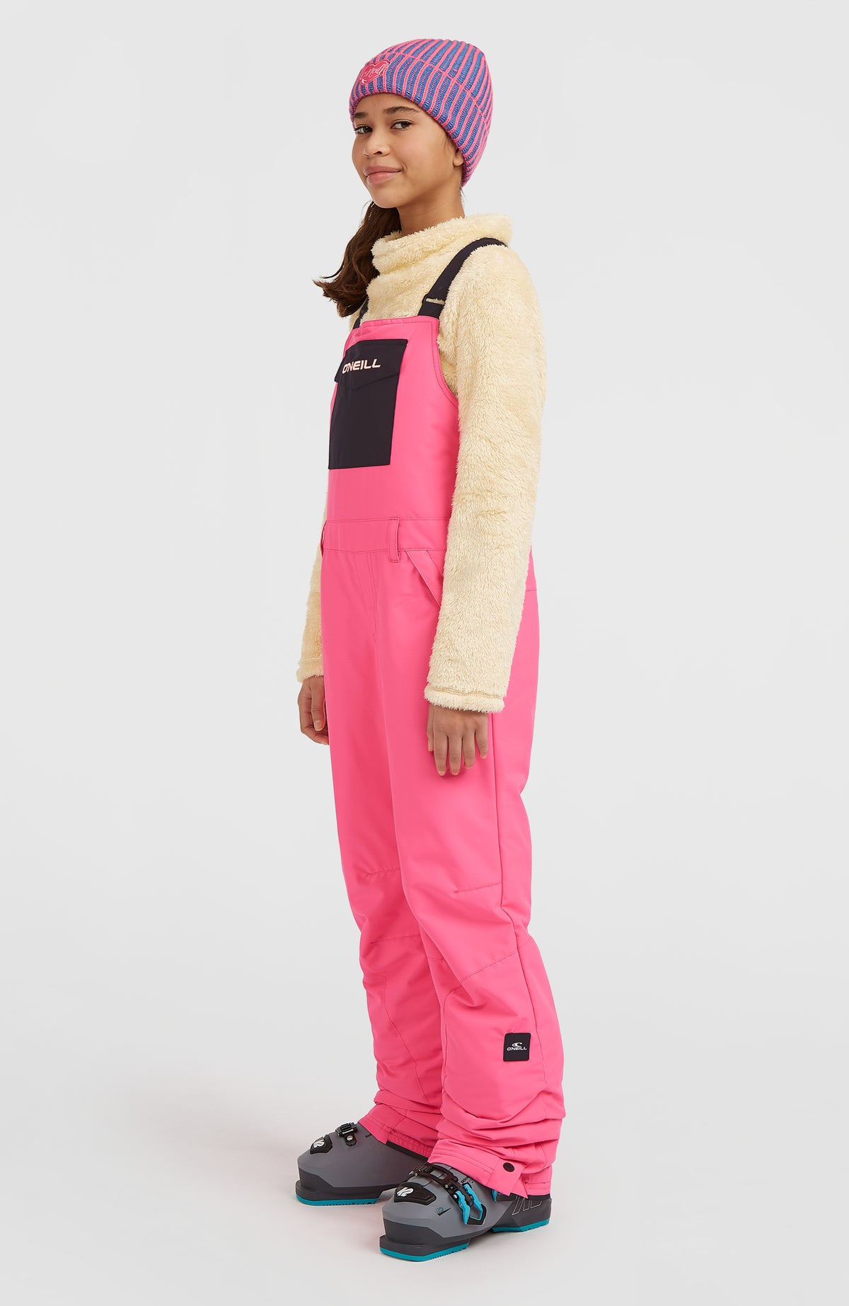 FWC'Cruz Bib Skihose für Kinder, pink, getragen am Model, Seitenansicht mit sichtbarem Logo-Patch am Saum