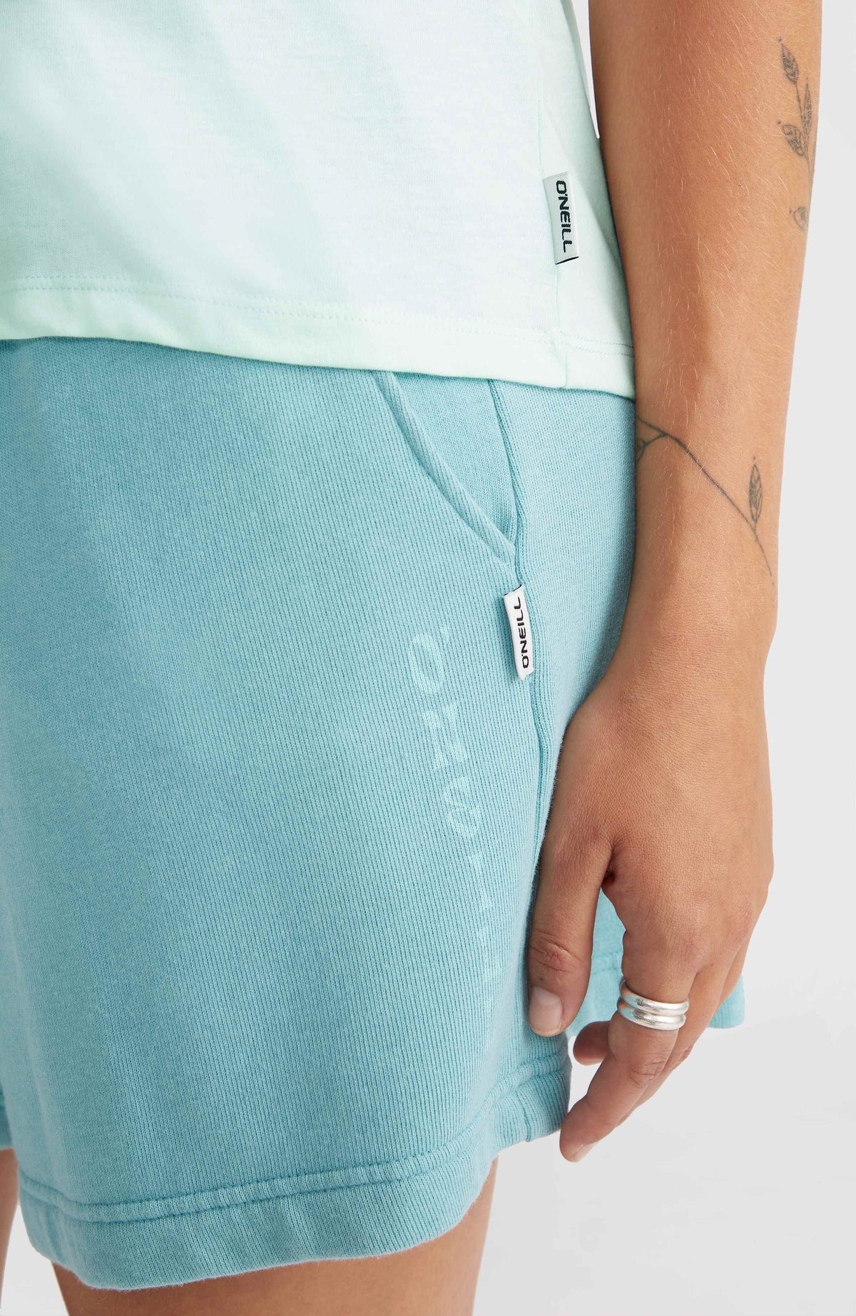 Essentials Racerback-Tanktop für Damen, blau, Nahaufnahme des unteren Saums mit seitlichem Logo-Label