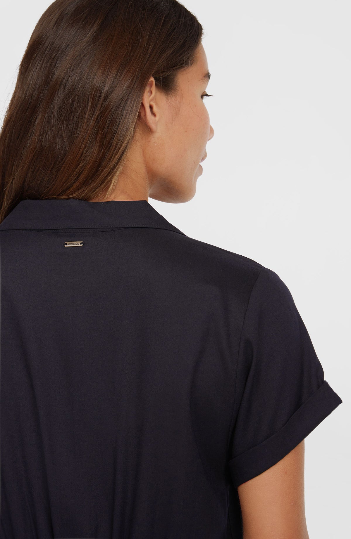 Women of the Wave Romper für Damen, schwarz, Nahaufnahme am Model mit kleinem Logo-Badge unterhalb des Kragens