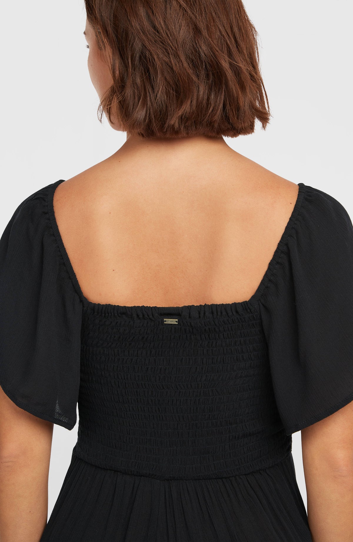 Kesia Jumpsuit, schwarz, Rückansicht am Model, gesmokter Einsatz mit kleinem Logo-Badge