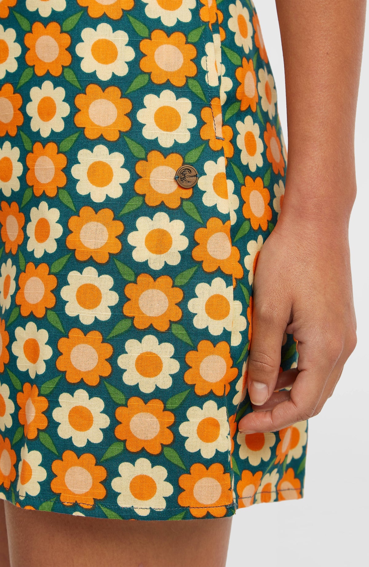 Nahaufnahme von Saum und kleinem Logo-Badge am grünen O'Riginals Playsuit mit Blumenmuster in Orange und Gelb
