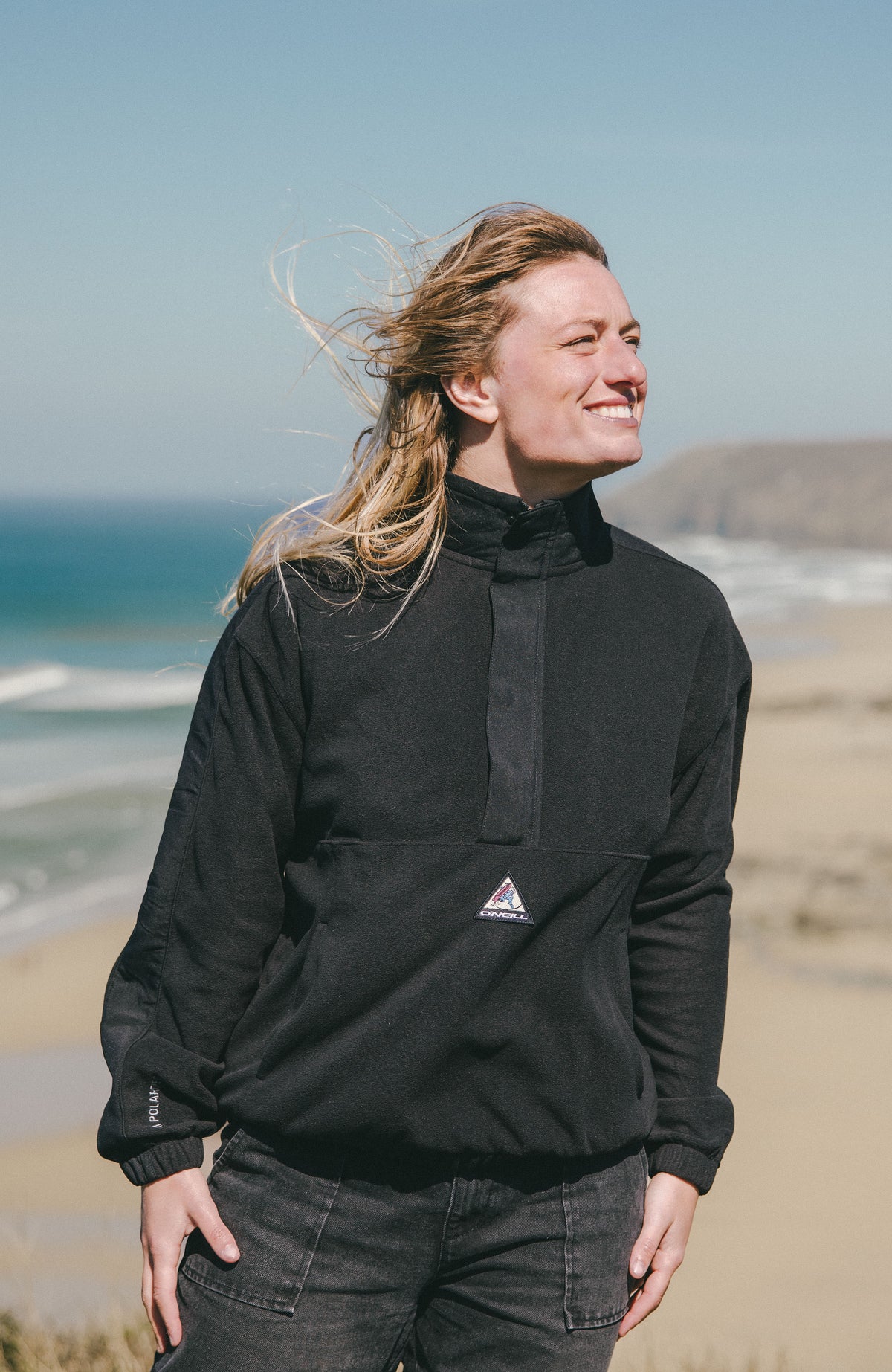 FWC'Play Polartec® Fleecepullover für Damen, schwarz, getragen am Model an der Küste mit Stehkragen