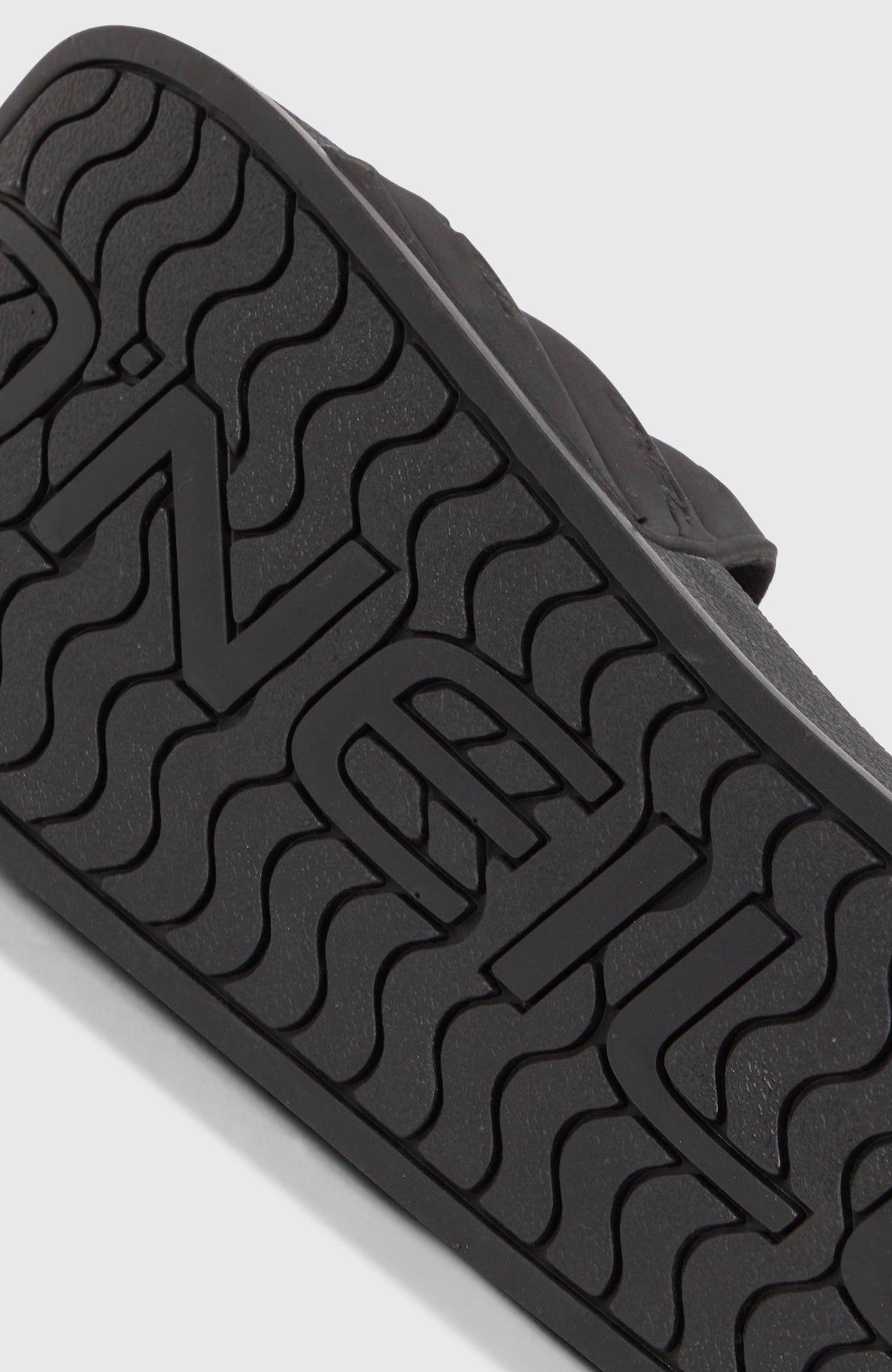 Nahaufnahme der gemusterten Sohle der schwarzen Slides