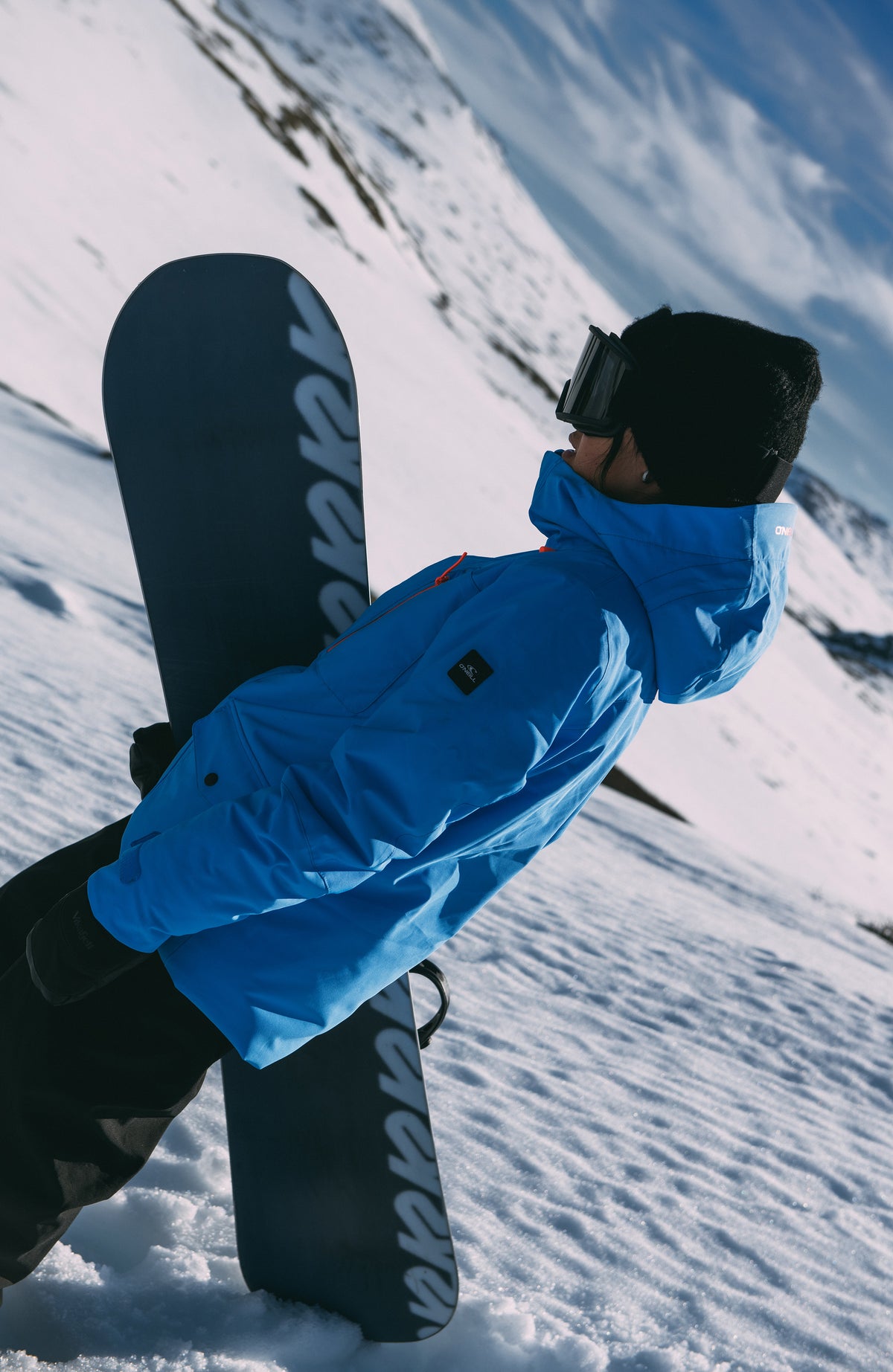 Blaue FWC'Peak Skijacke für Damen, im Schnee von der Seite mit Snowboard
