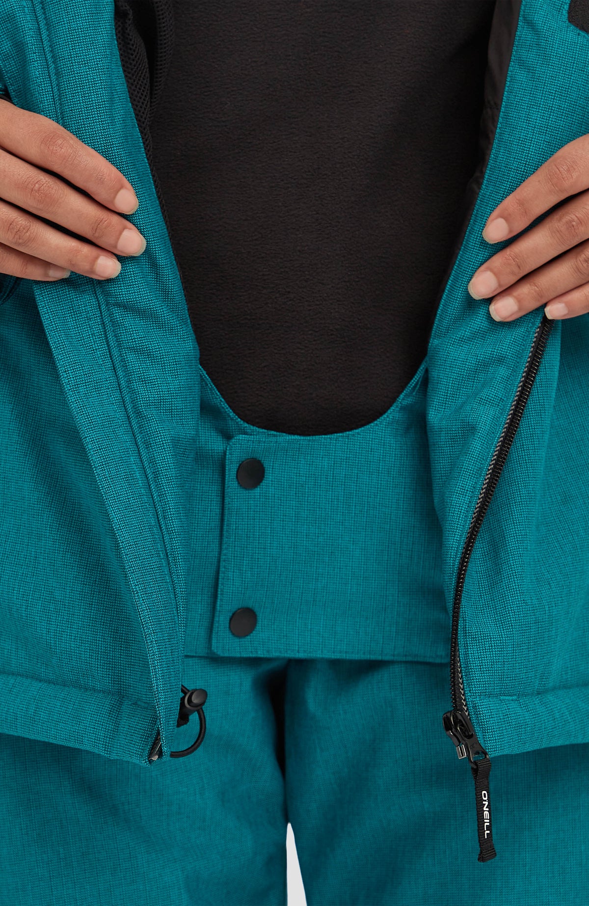 Nahaufnahme der blauen FWC'Cruz Melange Skijacke für Damen am Model, geschlossener Schneefang mit Druckknöpfen