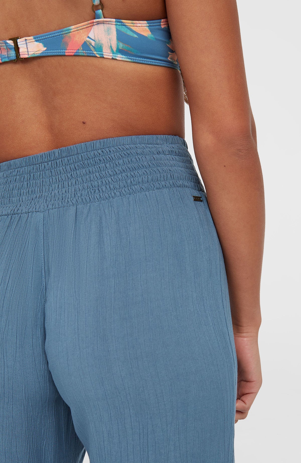 Nahaufnahme des gesmokten Bundes der blauen Johnny Smocked Waist Hose mit dezentem Metall-Logo