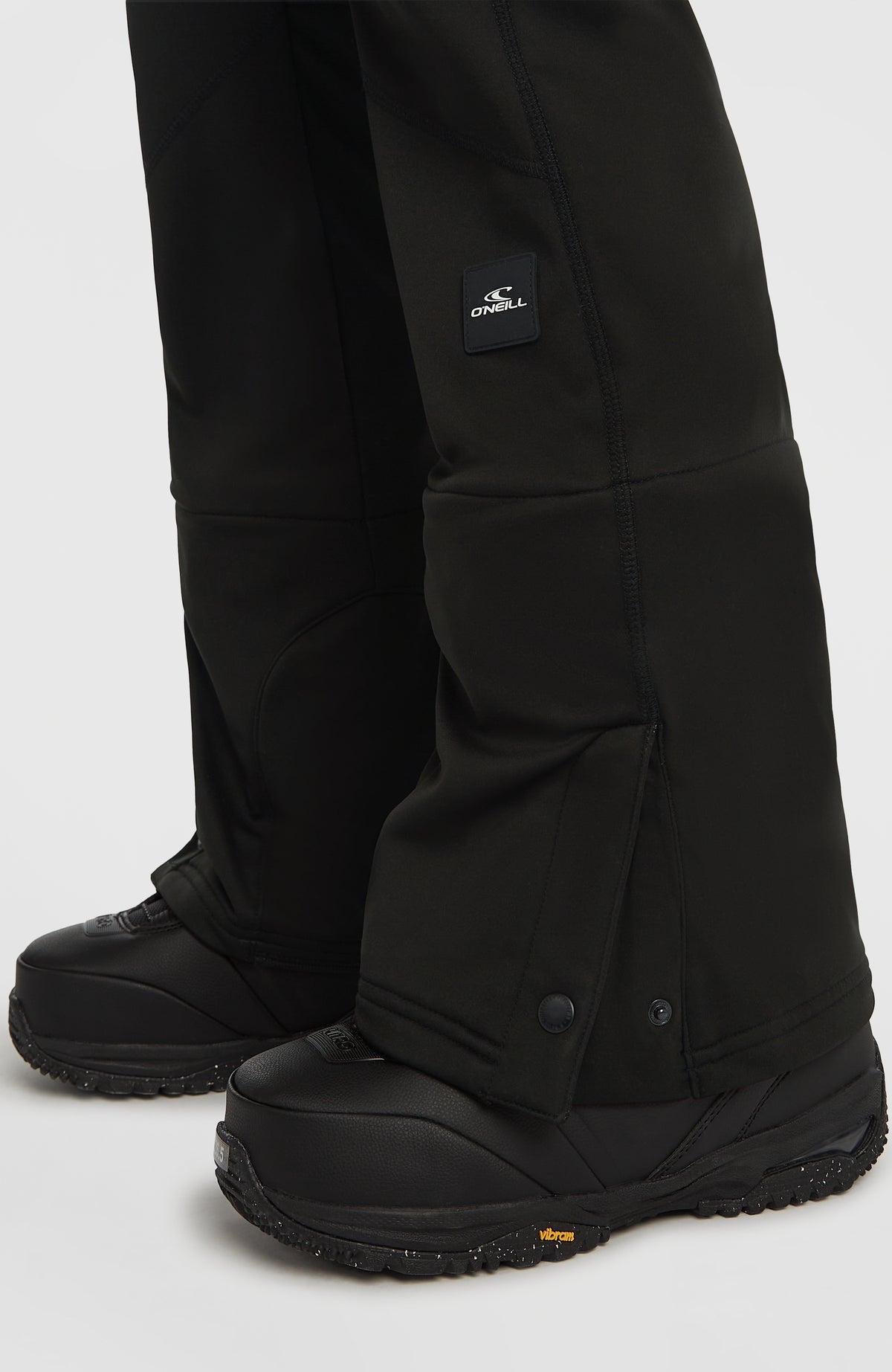 Nahaufnahme vom Hosenbeinsaum mit Druckknopf und Logo der schwarzen FWC'Cruz Softshell-Skihose am Model