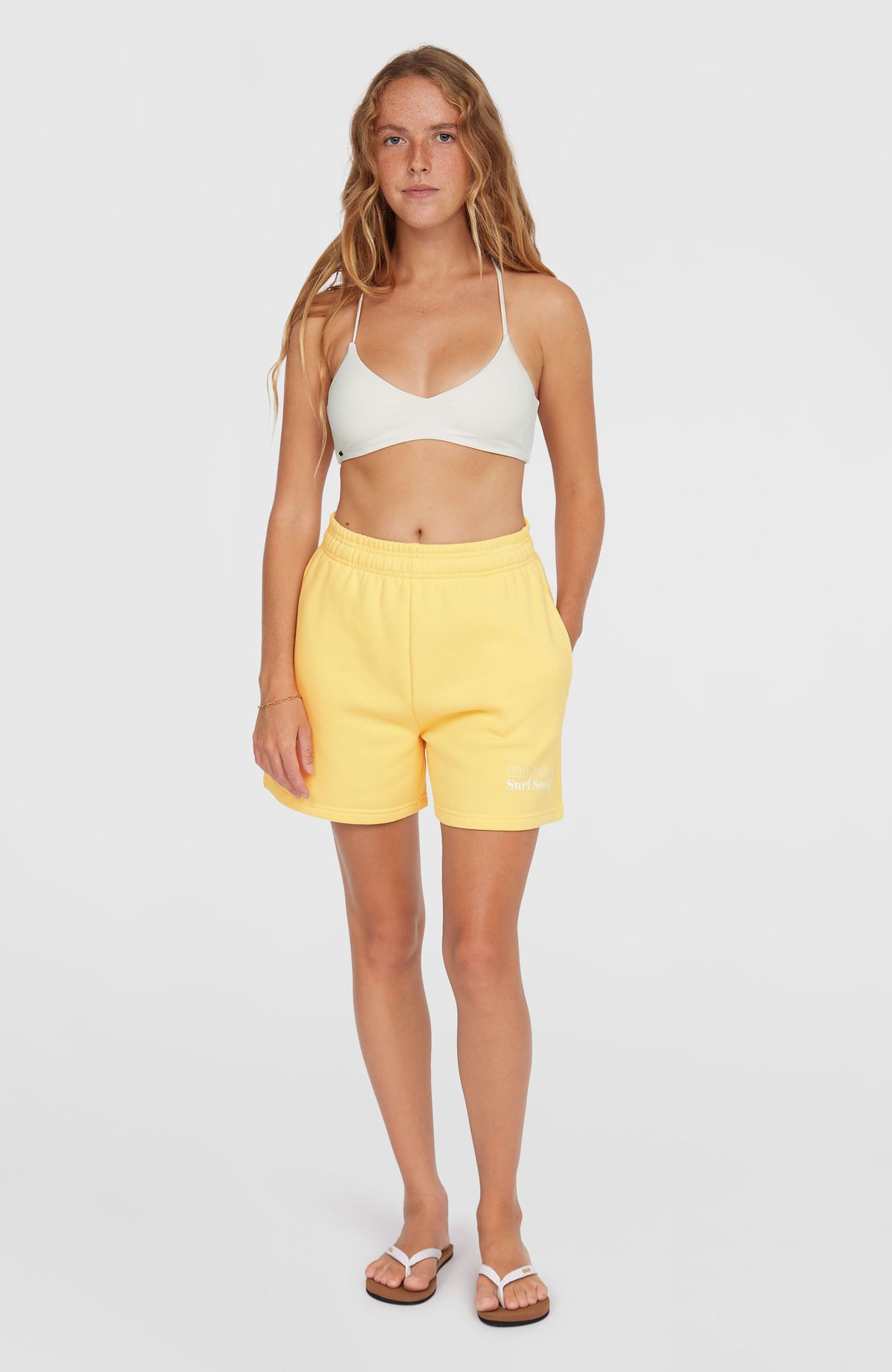 Future Surf Society Shorts für Damen, gelb mit Logo-Print in Weiß, Ganzkörperansicht von vorne getragen am Model