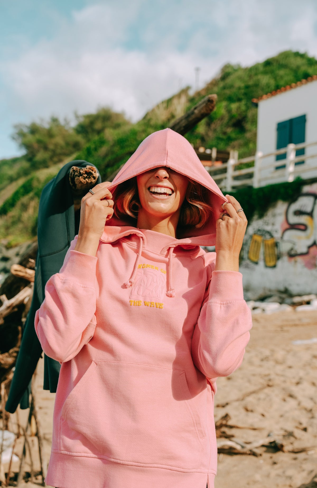 Women of the Wave Hoodie für Damen, pink mit Grafik-Print in Gelb, am Strand getragen mit aufgesetzter Kapuze