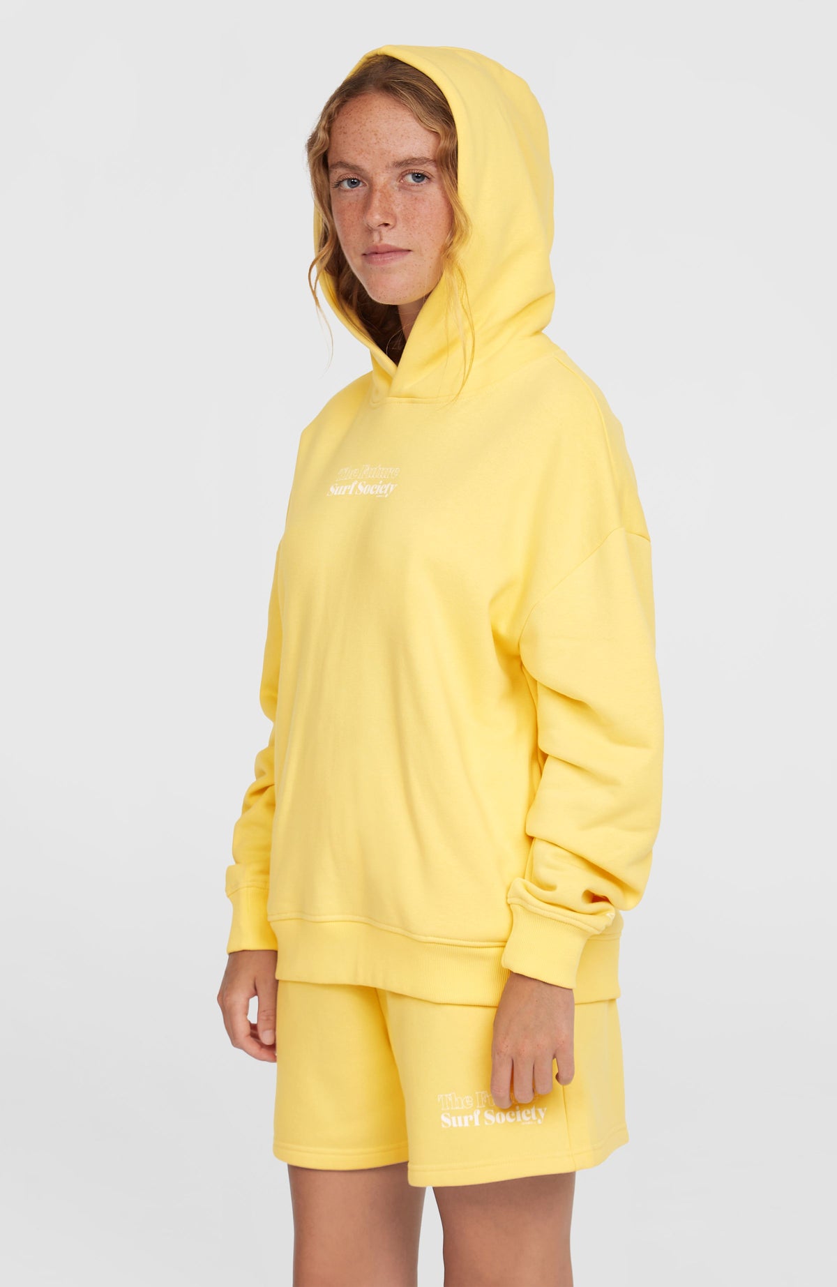 Future Surf Society Hoodie für Damen, gelb mit Schriftzug-Print in Weiß, Halbprofilansicht mit aufgesetzter Kapuze