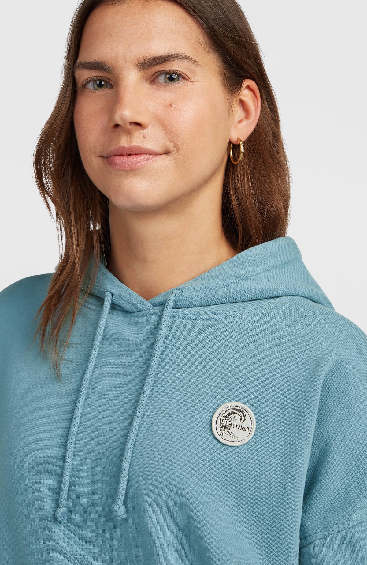 Nahaufnahme des blauen O'Riginals Badge Hoodie mit Kordelzug und rundem Logo-Badge auf der Brust