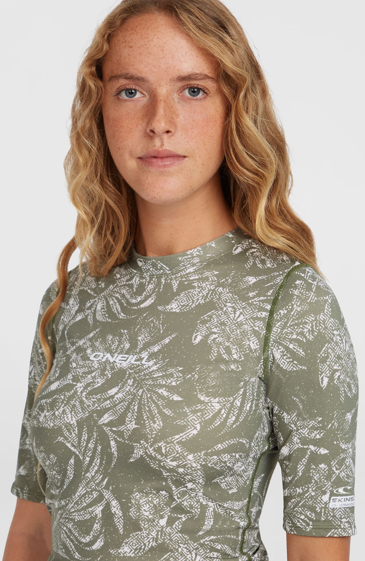 Essentials Shortsleeve-Schwimmshirt, grün mit Pflanzenmuster in Weiß, Nahaufnahme mit Logo-Print am Halsausschnitt