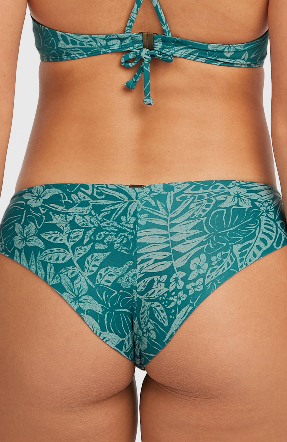 Nahaufnahme der grünen Maoi Bikinihose mit Pflanzenmuster in Hellgrün, kleines Metall-Logo am Bund hinten
