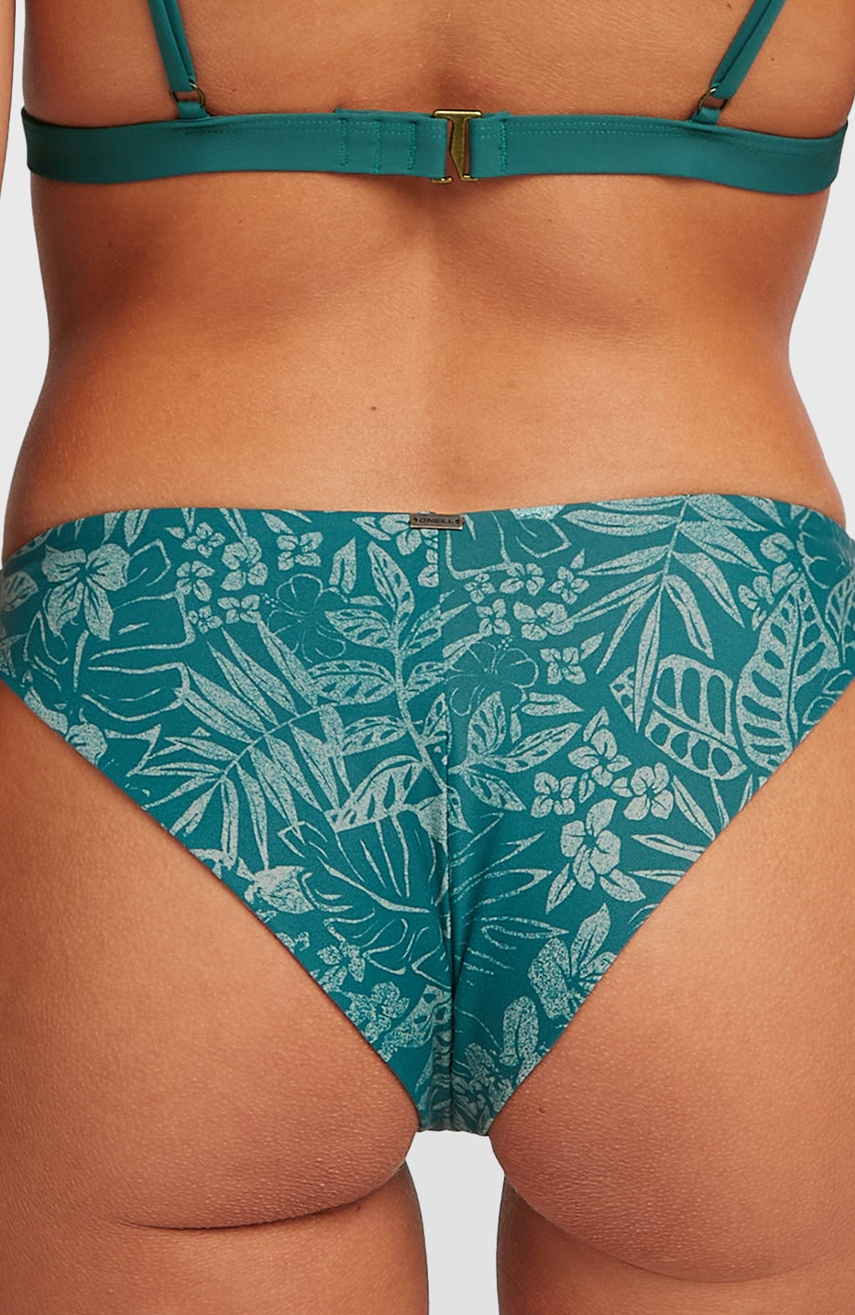 Nahaufnahme der grünen Amy Bikinihose mit Pflanzenmuster in Hellgrün, Rückseite mit Logo-Badge am Bund