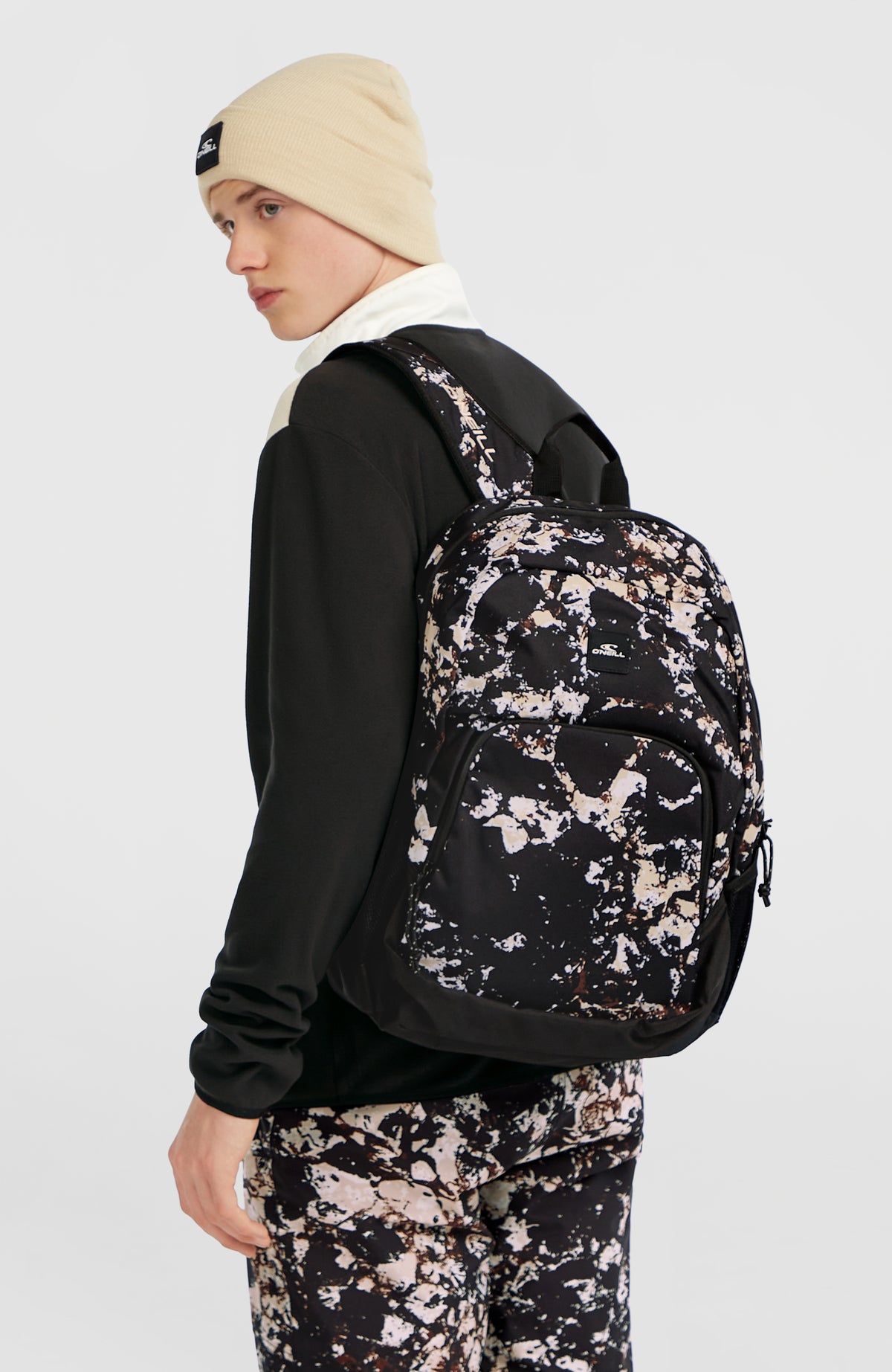 Wedge Rucksack für Herren, schwarz mit Allover-Print in Beige und Weiß, getragen am Model in Seitenansicht