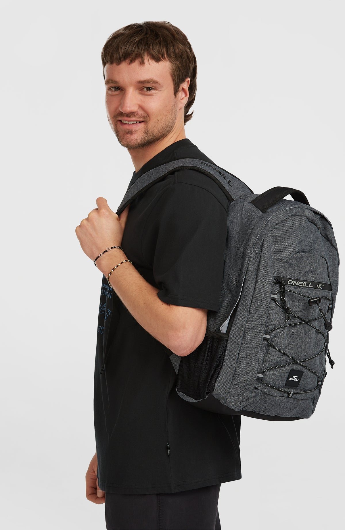Kleiner Boarder Rucksack für Herren, grau, getragen am Model in Seitenansicht mit Schultergurt und Netzfach