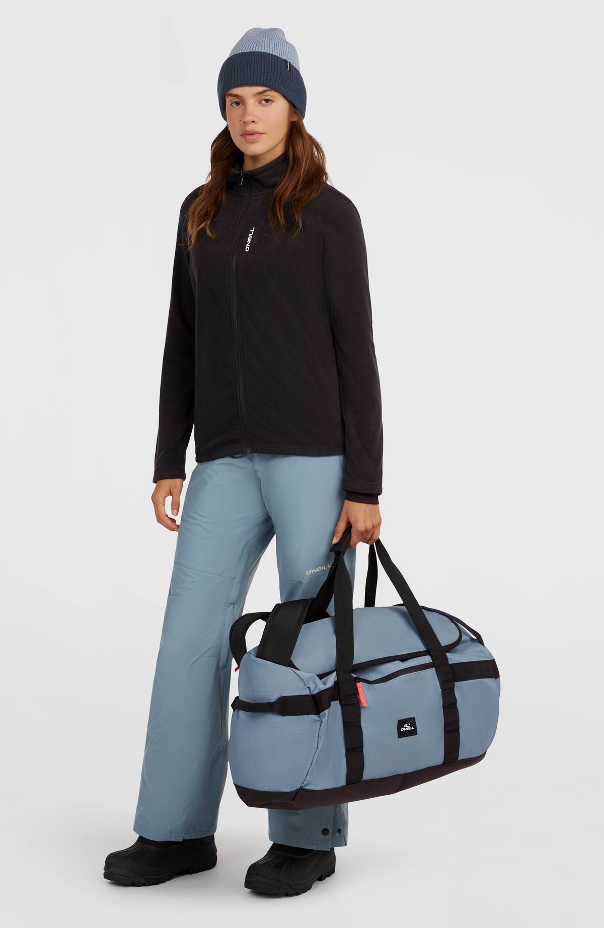 Blaue Reisetasche, getragen am Model in Ganzkörperansicht von vorne mit schwarzen Tragegriffen