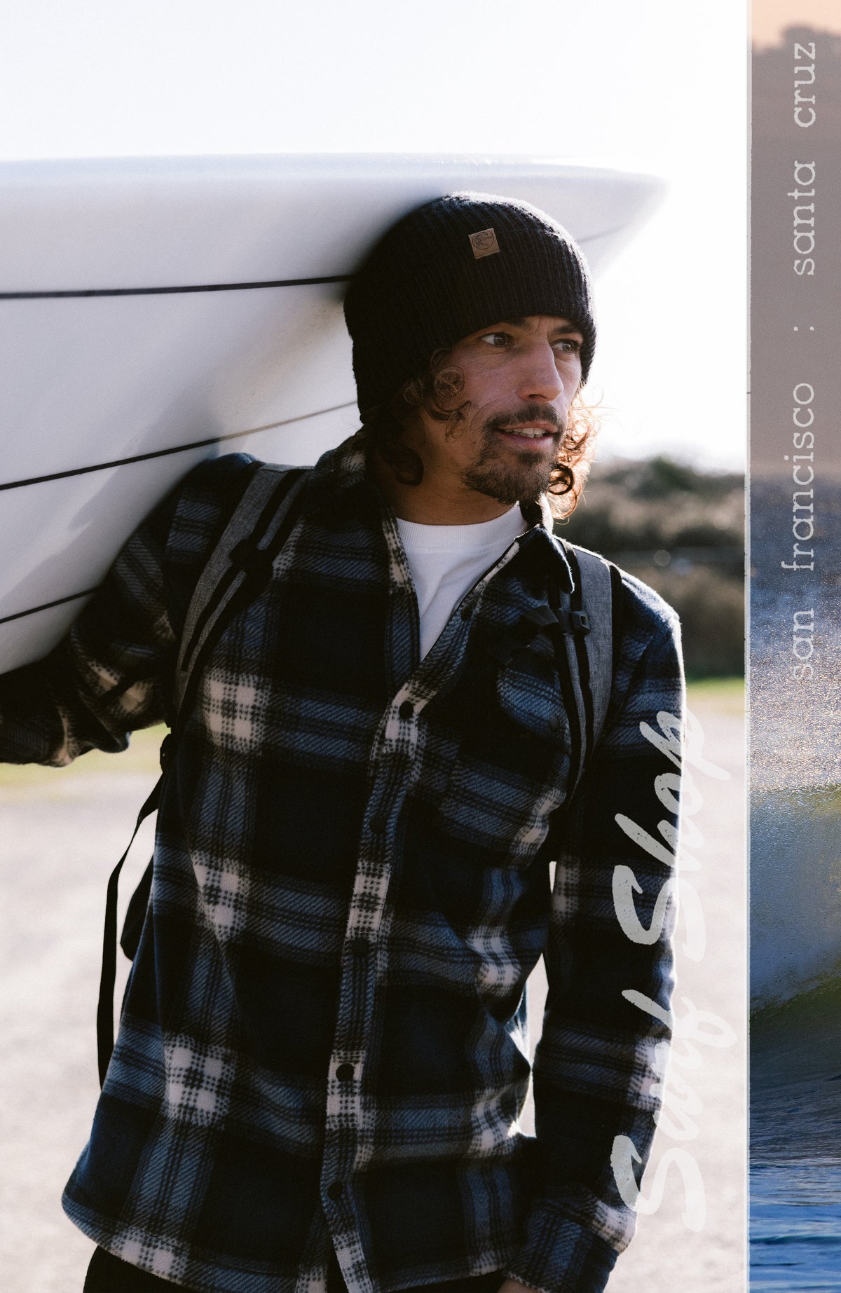 O'Riginals Superfleece Hemd für Herren, blau mit Karomuster in Weiß und Schwarz, an der Küste mit Surfbrett am Model
