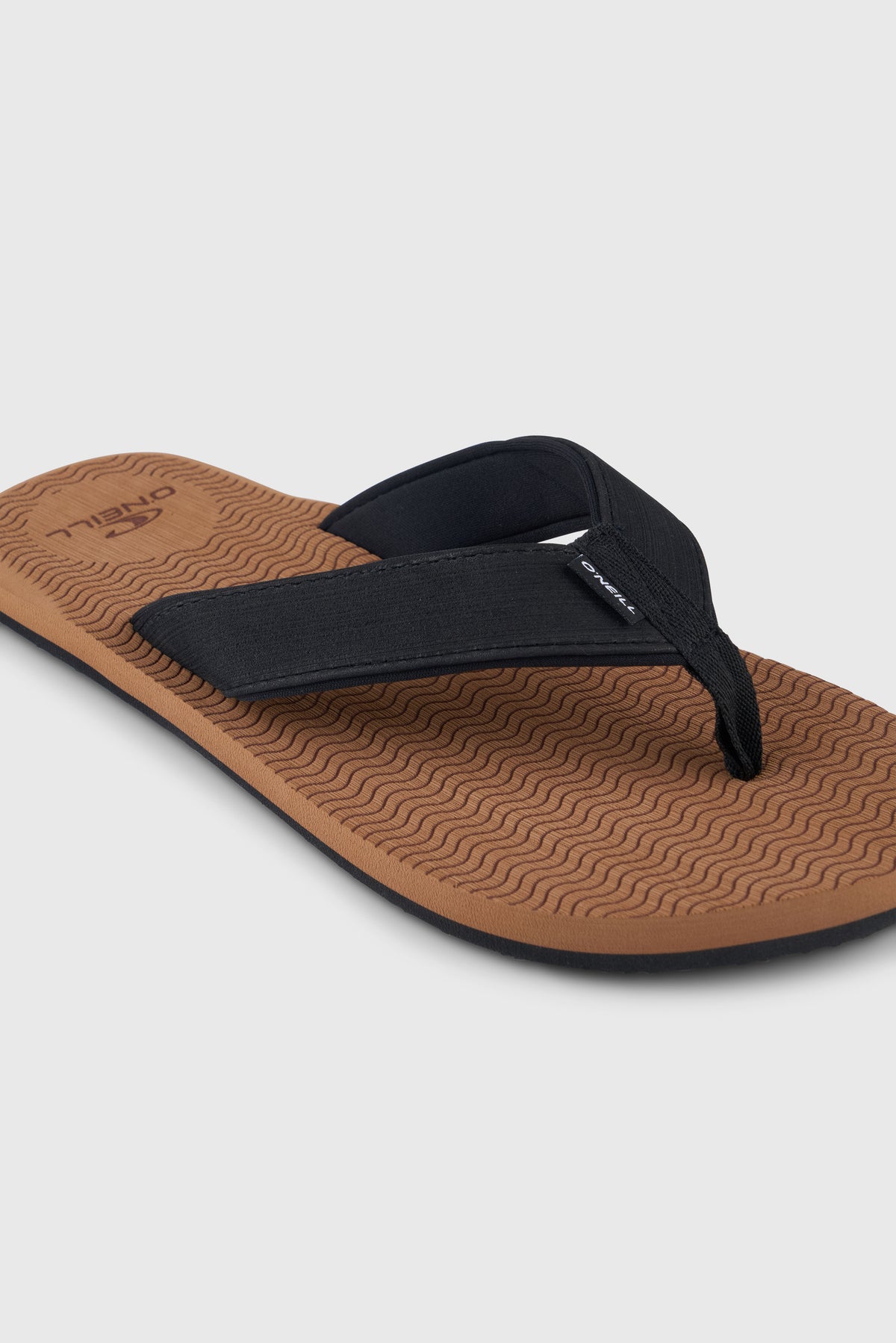 Nahaufnahme der braunen Koosh Sandalen mit schwarzem Riemen und Logo-Fähnchen