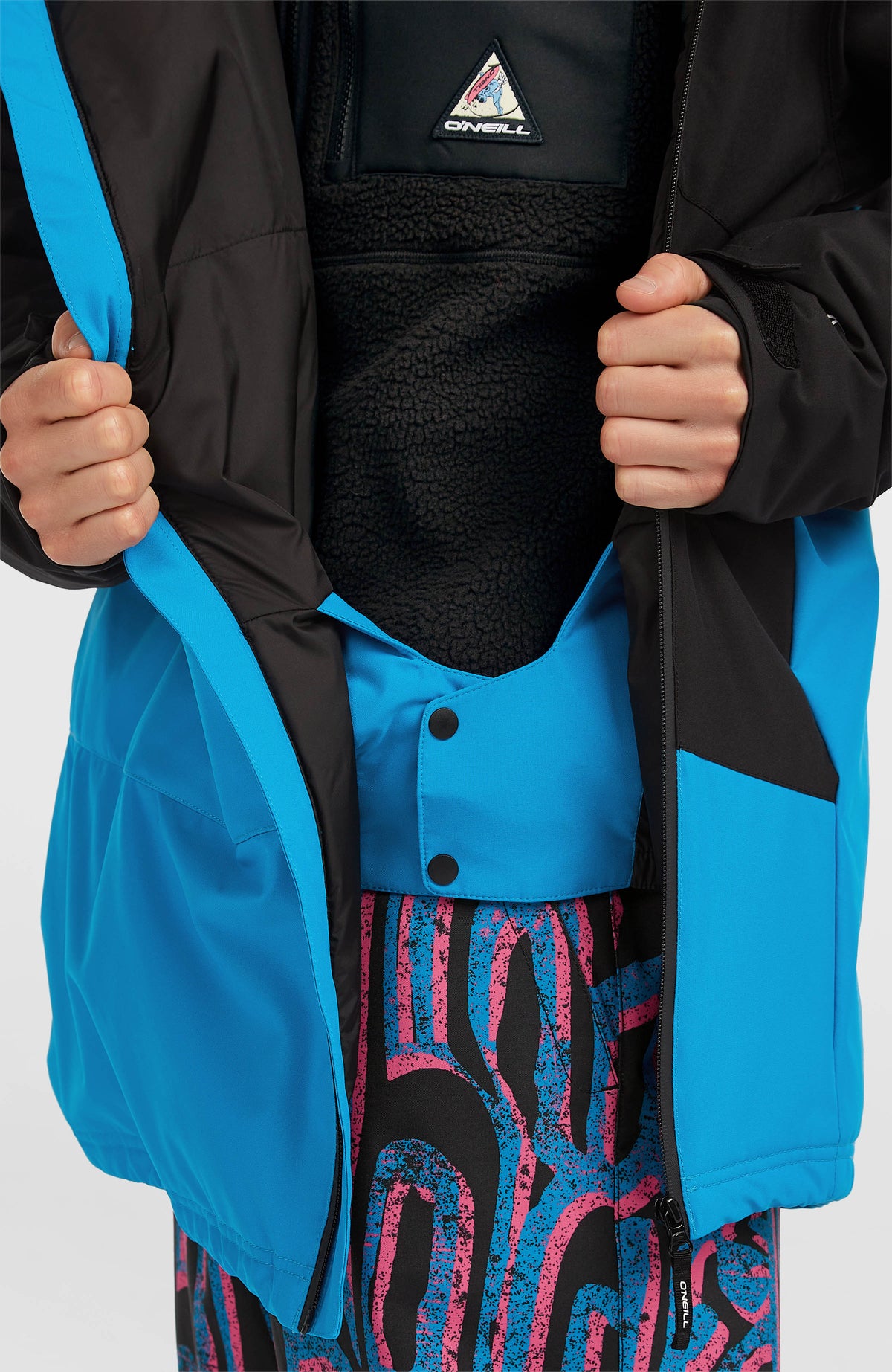 Nahaufnahme der blauen FWC'Play Asymmetric Ski- und Snowboardjacke mit Schneefang und Druckknöpfen
