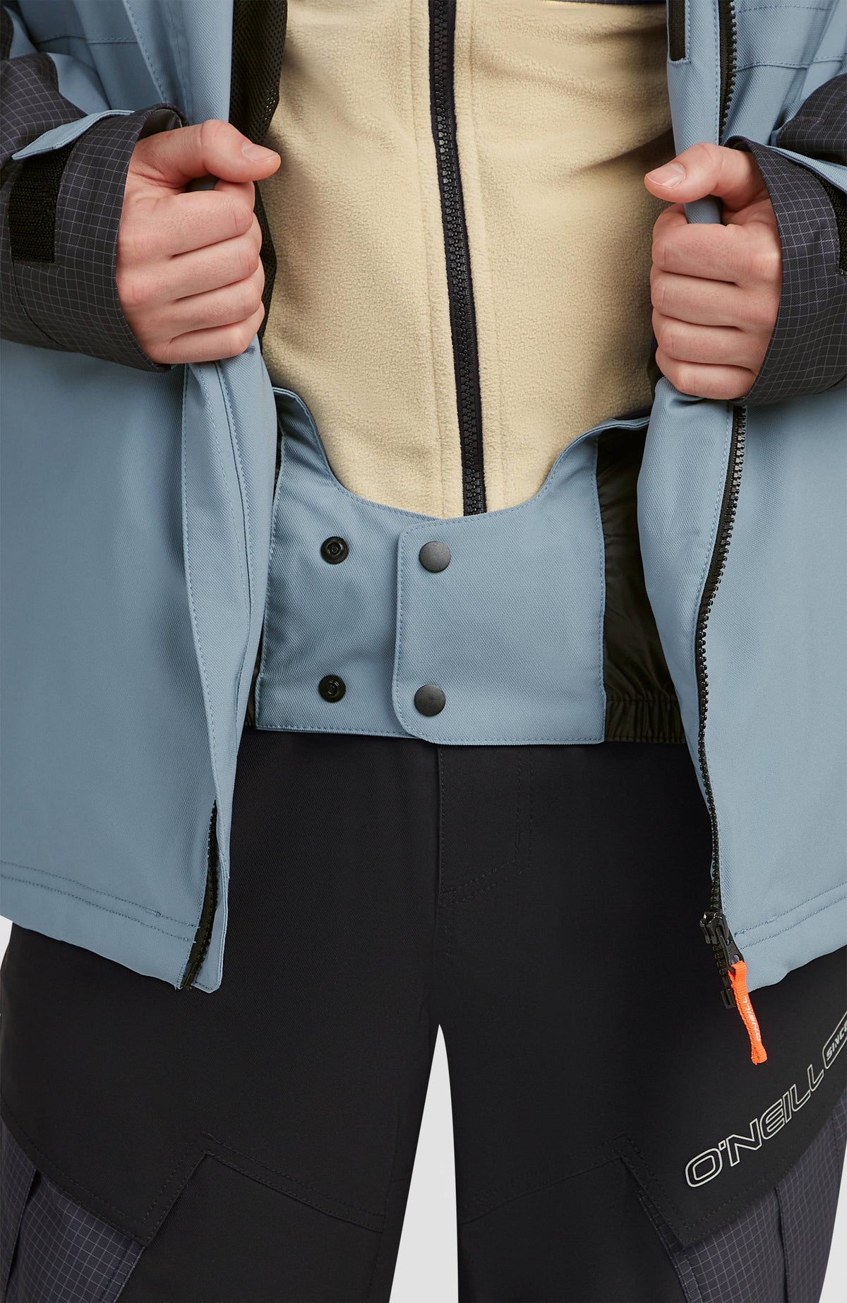 Nahaufnahme des geschlossenen Schneefangs mit Druckknöpfen der blauen FWC'Peak Skijacke für Herren am Model
