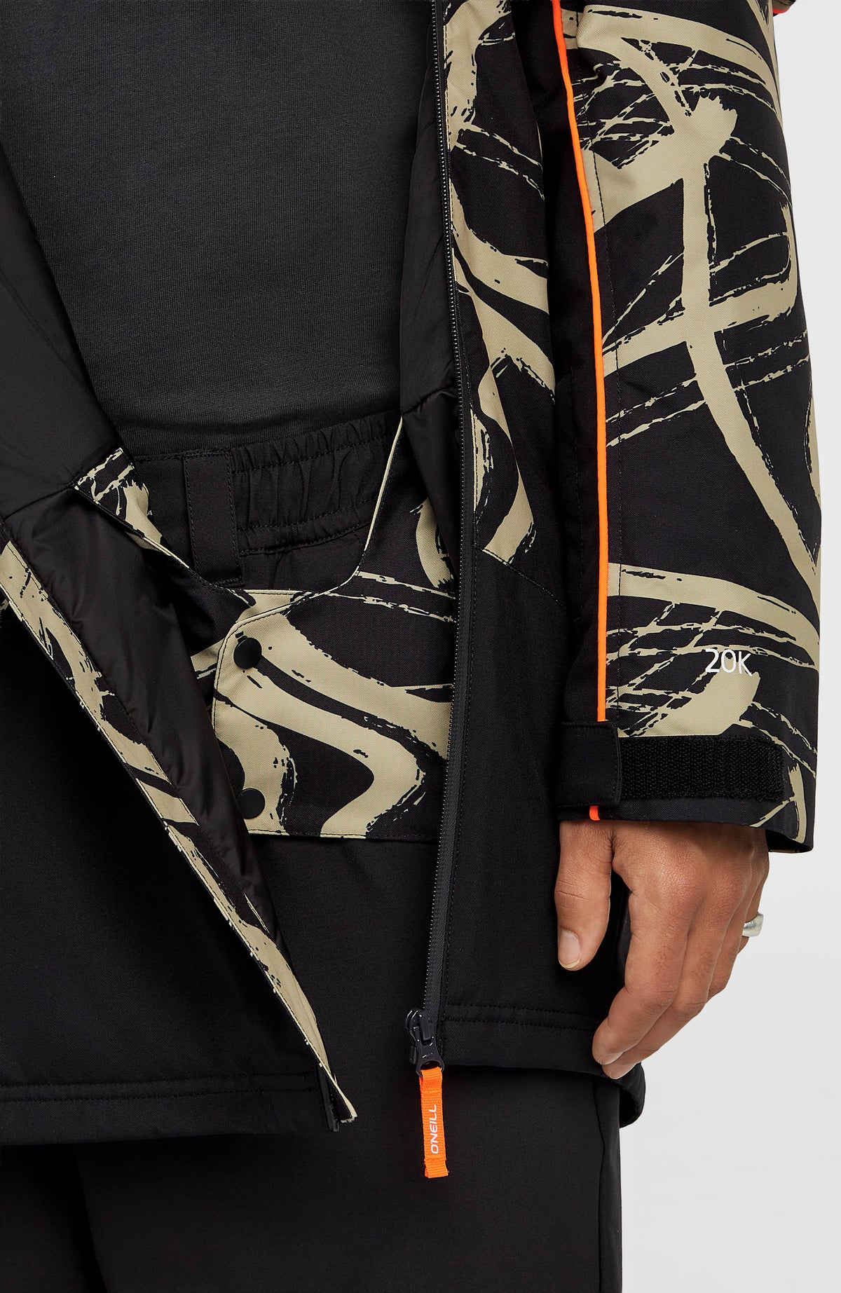 Nahaufnahme von Schneefang und Saumreißverschluss der beigen FWC'Play Asymmetric Ski- und Snowboardjacke