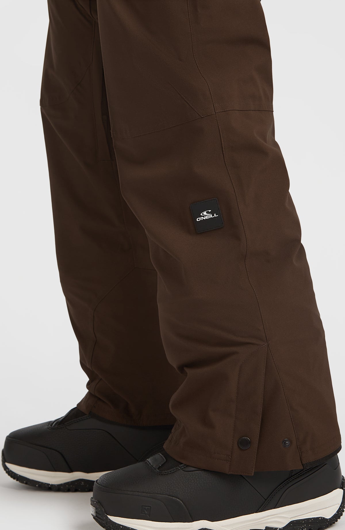 Nahaufnahme von Hosenbein, Saumknöpfen und Logo-Patch der braunen FWC'Peak Fire Skihose am Model
