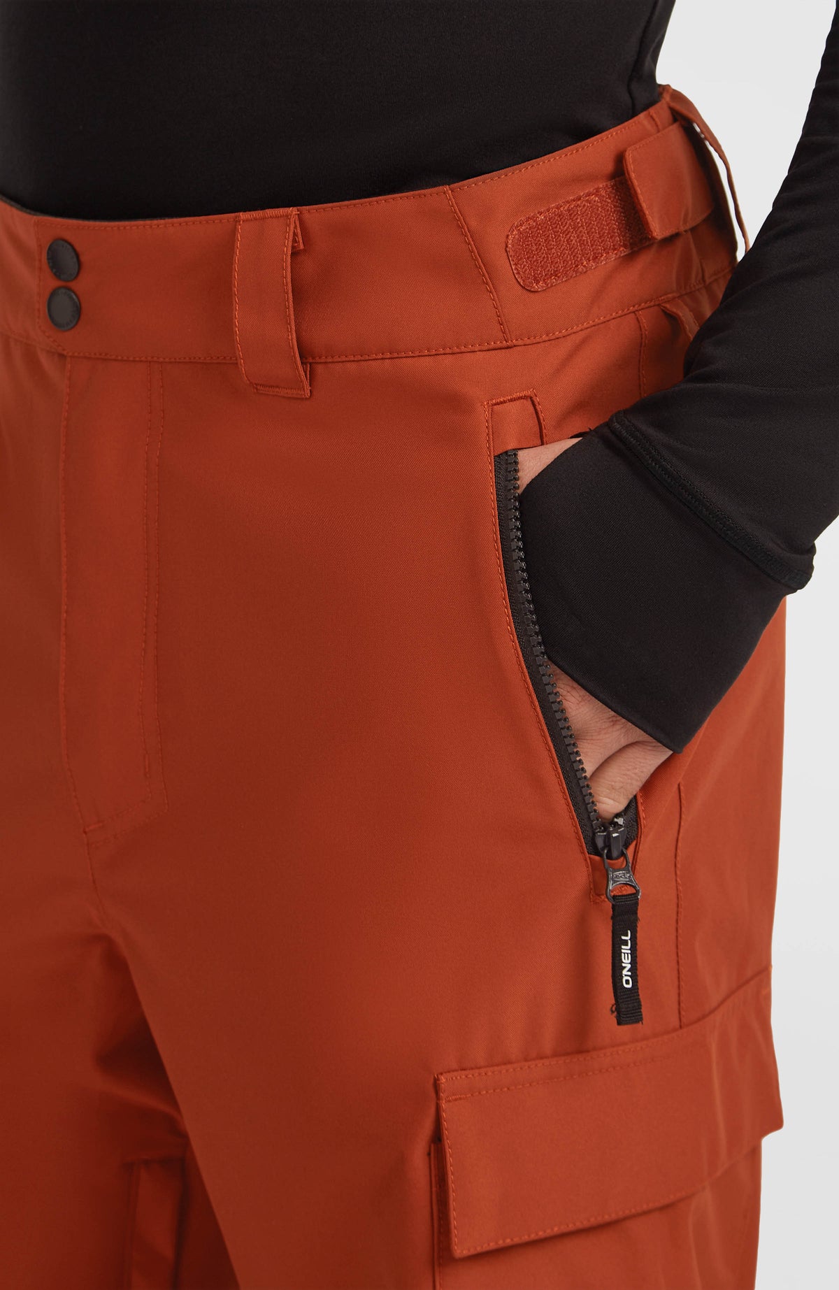 Nahaufnahme der seitlichen Reißverschlusstasche und des verstellbaren Bundes der orangen FWC'Cruz Cargo-Skihose