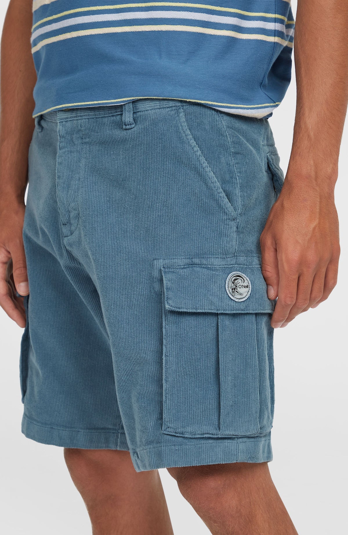 Nahaufnahme der blauen O'Riginals Cord-Cargo-Shorts am Model, seitliche Tasche mit rundem Logo-Badge
