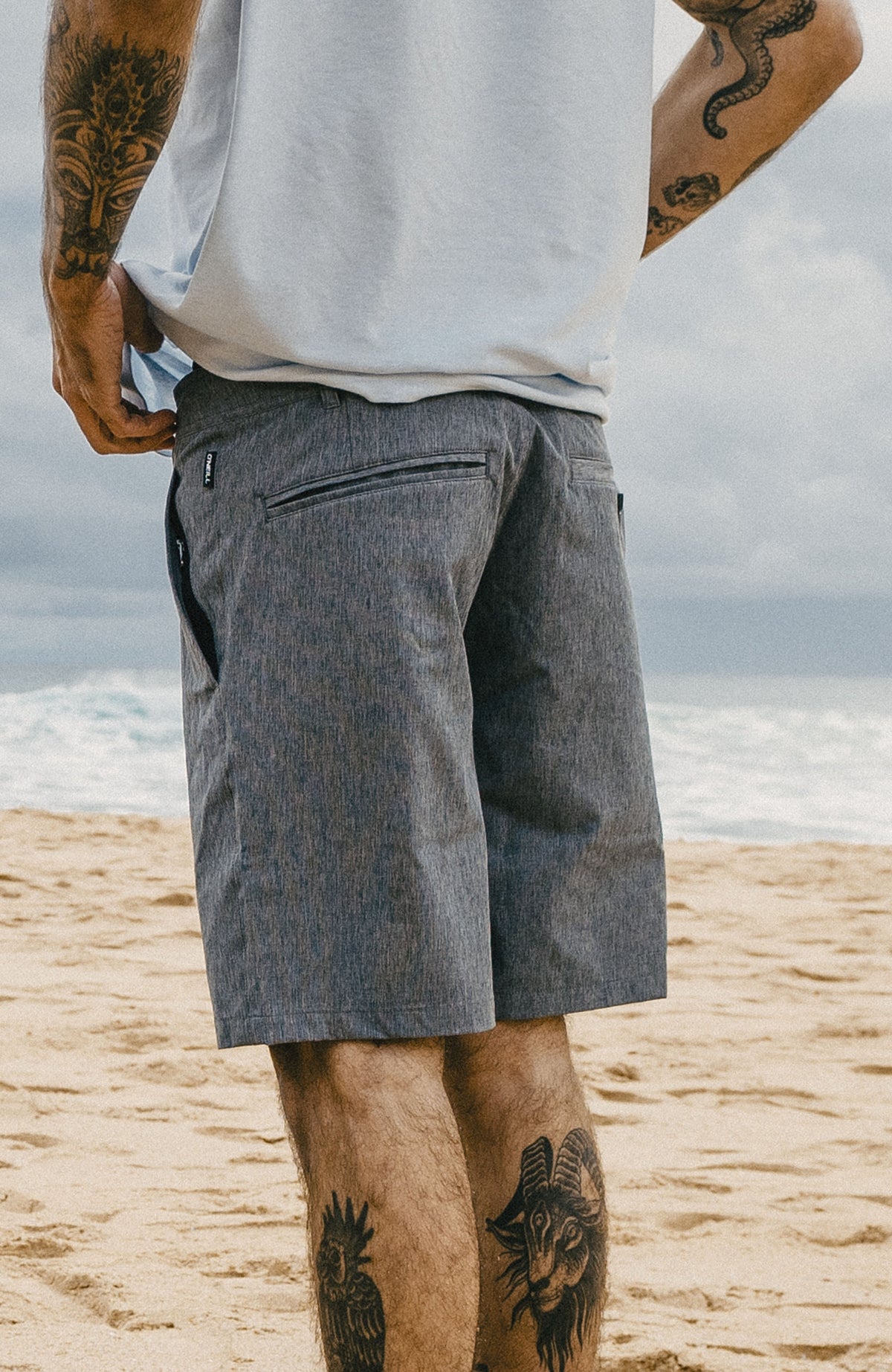 Schwarze Hybrid 19" Melange Shorts für Herren, am Strand getragen, schräge Rückansicht mit Paspeltasche