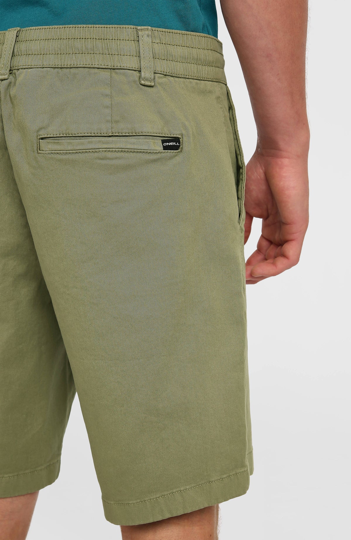 Nahaufnahme der grünen Essentials Chino-Shorts am Model, Gesäßtasche mit kleinem Logo-Etikett am Bund