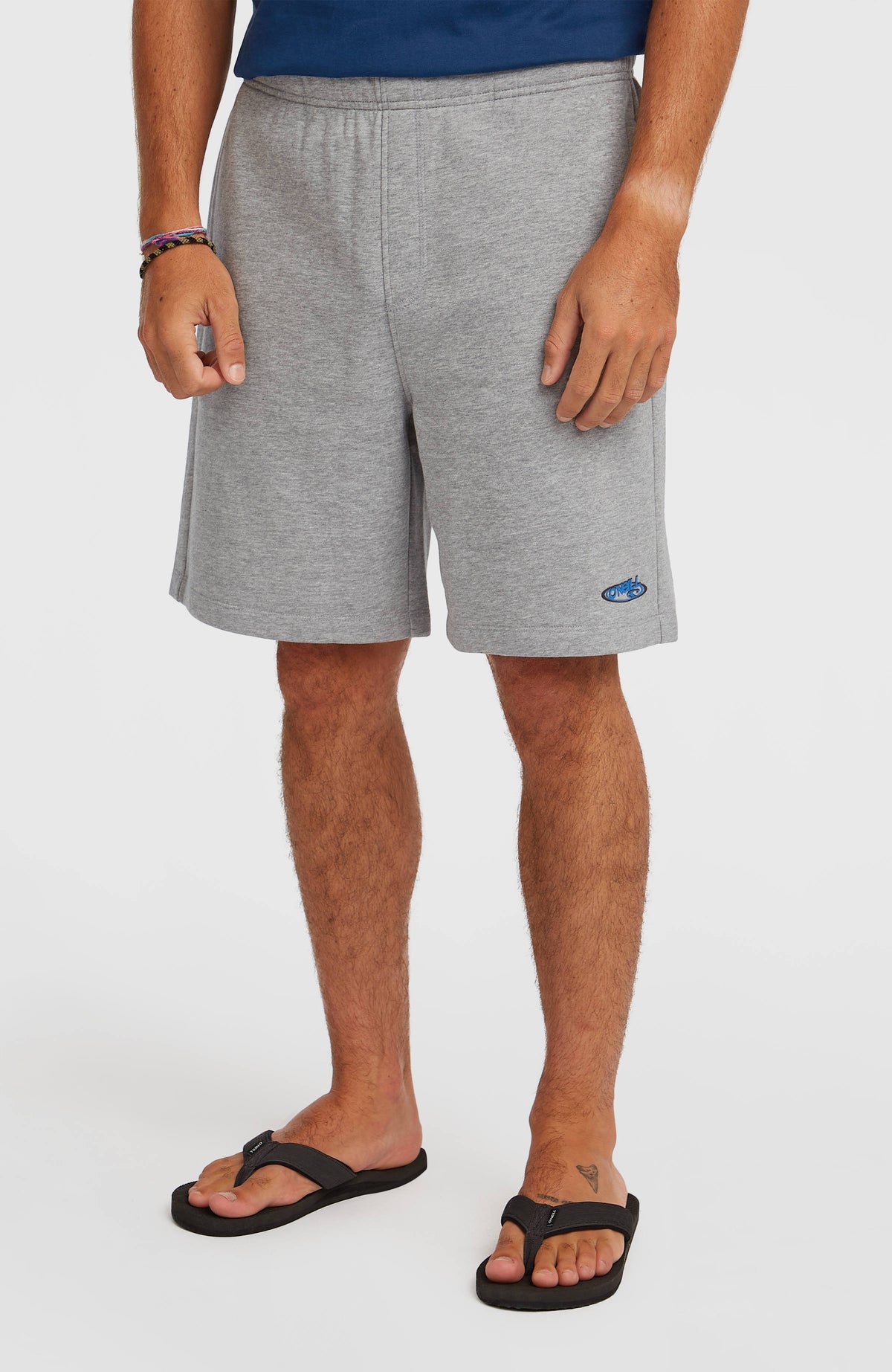 Essentials 90s Sweatshorts für Herren, grau, Vorderansicht am Model mit blauem Logo-Detail am unteren Saum