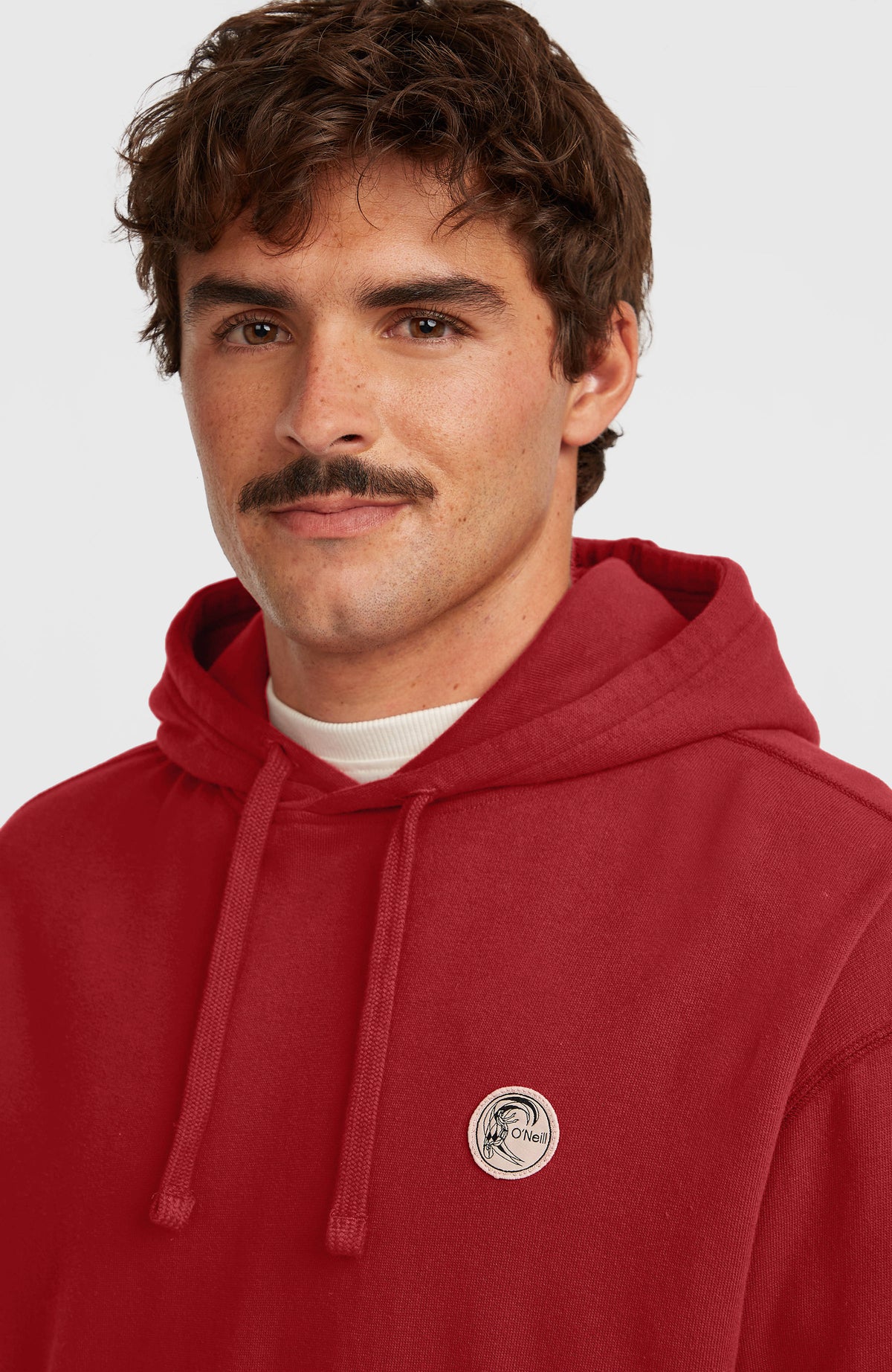 Nahaufnahme des roten O'Riginals Hoodie für Herren mit rundem Logo-Badge auf der Brust und Kordelzug