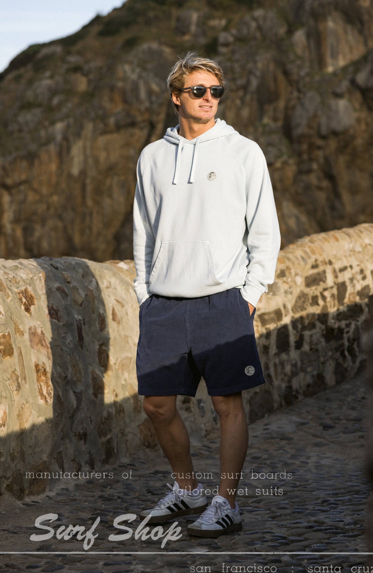 O'Riginals Badge Hoodie für Herren, blau, am Model auf einer Steinmauer im Freien