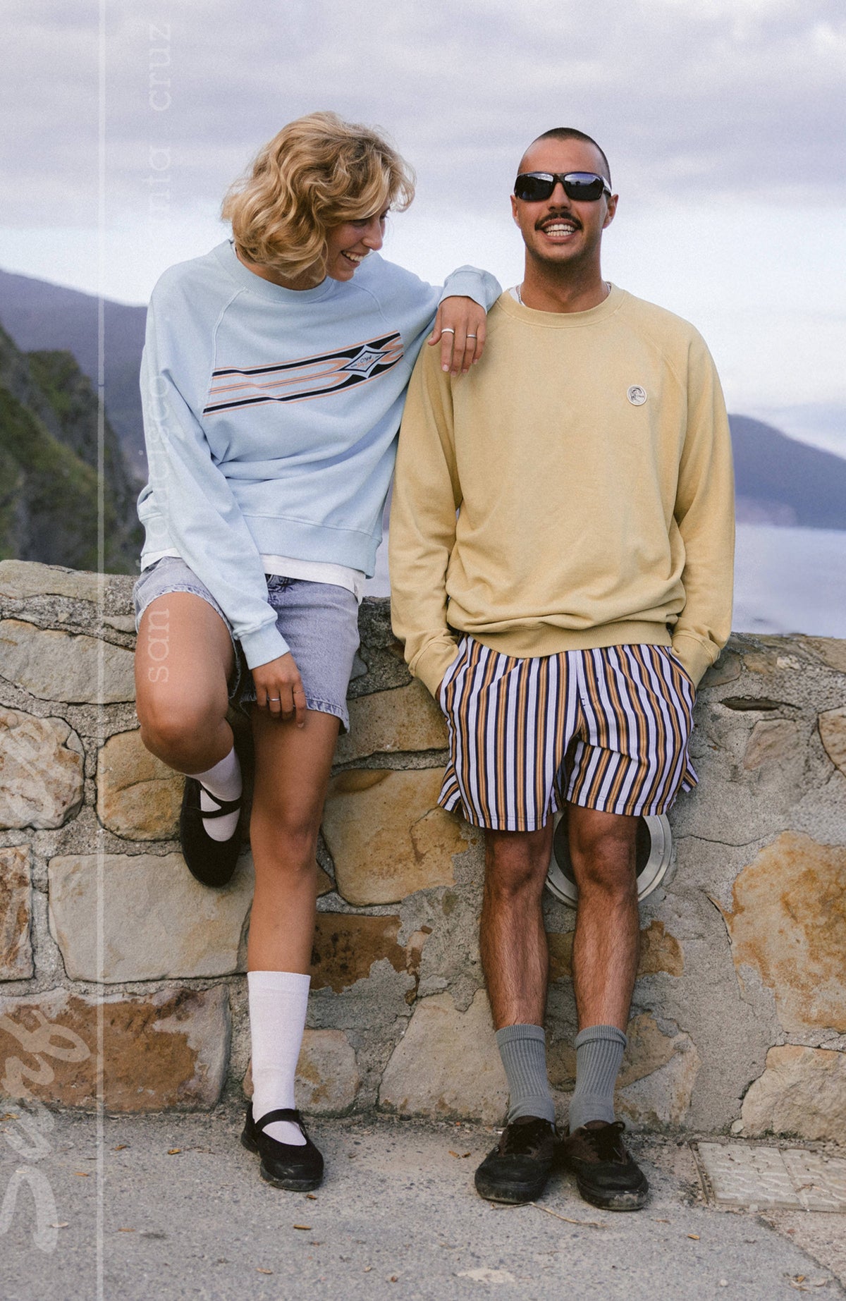 O'Riginals Badge Crew Sweatshirt für Herren in Beige, getragen an einer Steinmauer an der Küste