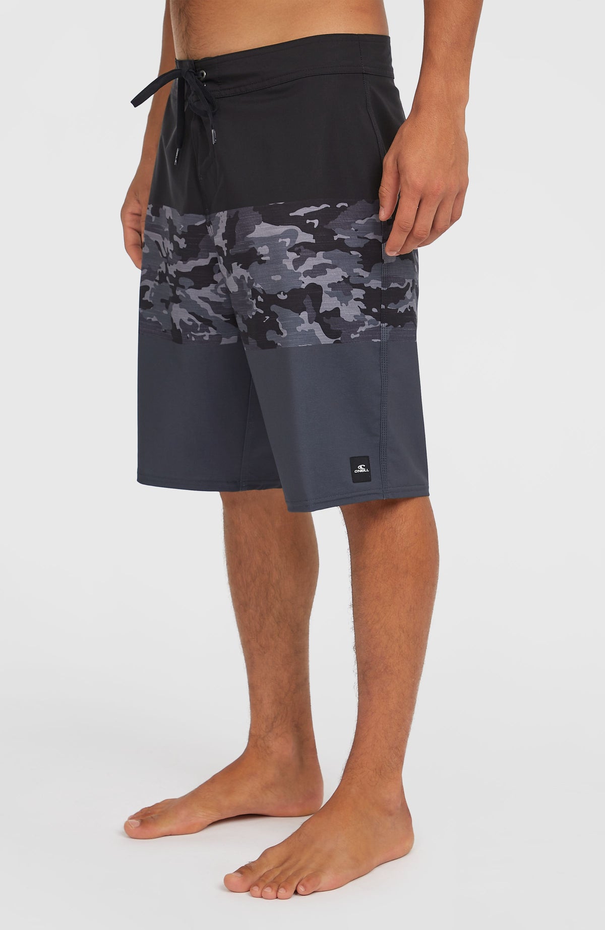Hyperfreak Heat Block 21'' Boardshorts, schwarz mit Camouflage-Muster in Grau, Seitenansicht am Model mit Logo-Patch am Saum