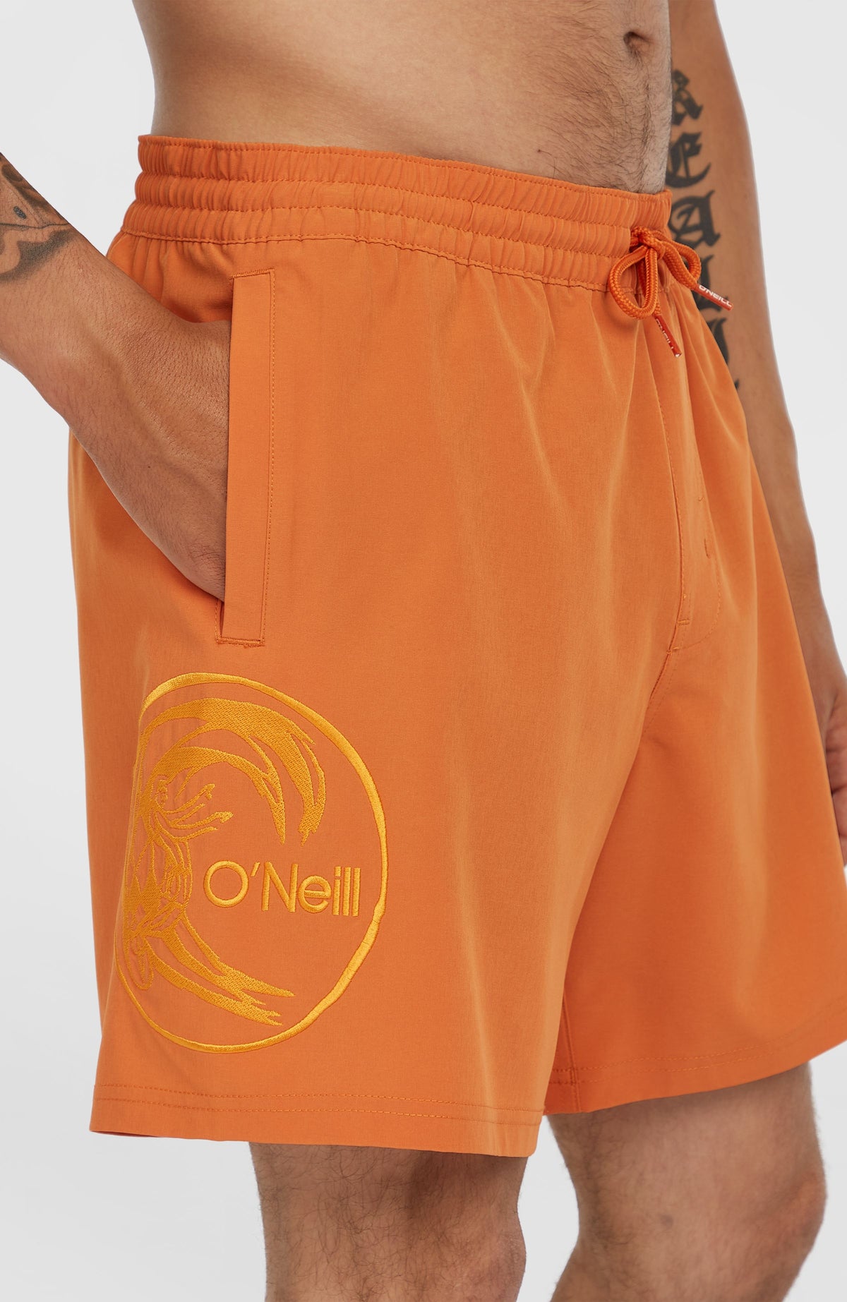 O'Riginals Cali Ocean 16'' Badehose für Herren, orange, Nahaufnahme am Model mit runder Logo-Stickerei am Hosenbein