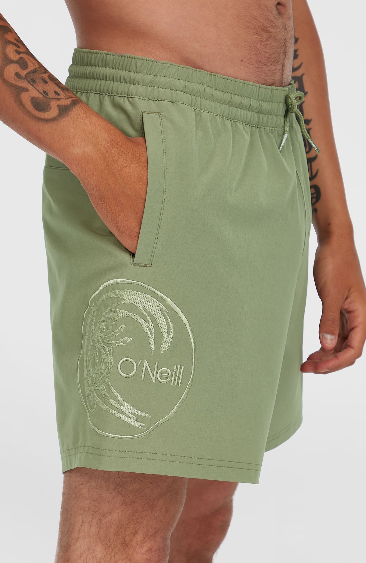 Nahaufnahme der grünen O'Riginals Cali Ocean 16'' Badehose mit runder Logo-Stickerei am Hosenbein