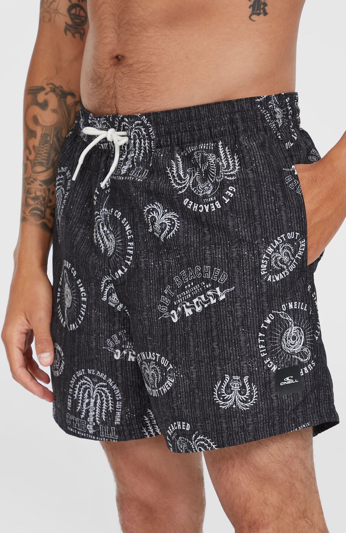 Nahaufnahme der Cali Print 15'' Badehose in Schwarz mit Grafik-Print in Weiß am Model, Detail der Seitentasche