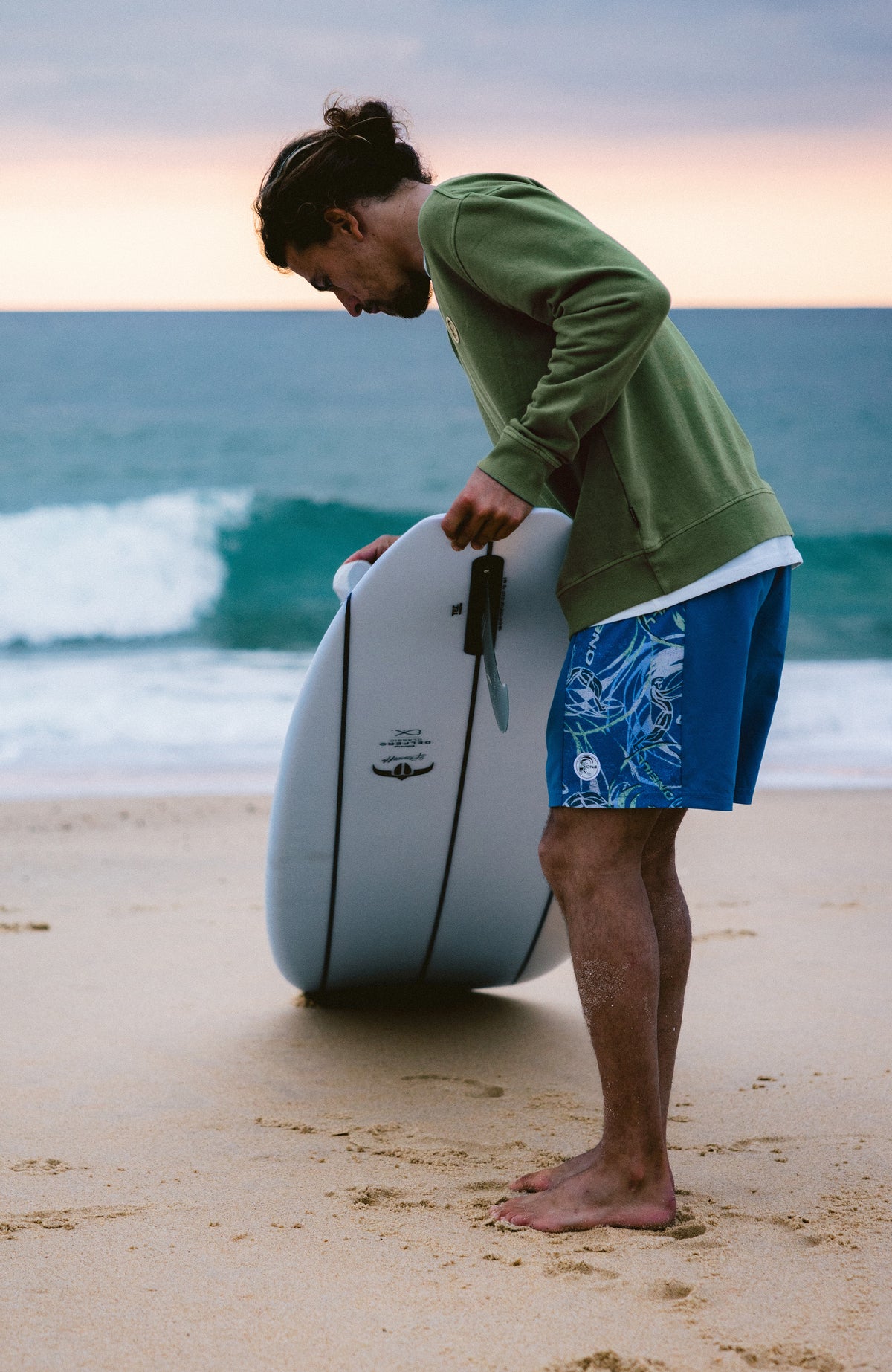 O'Riginals Side Panel 16'' Badehose für Herren, blau mit Grafikmuster in Weiß, getragen am Strand mit Surfbrett