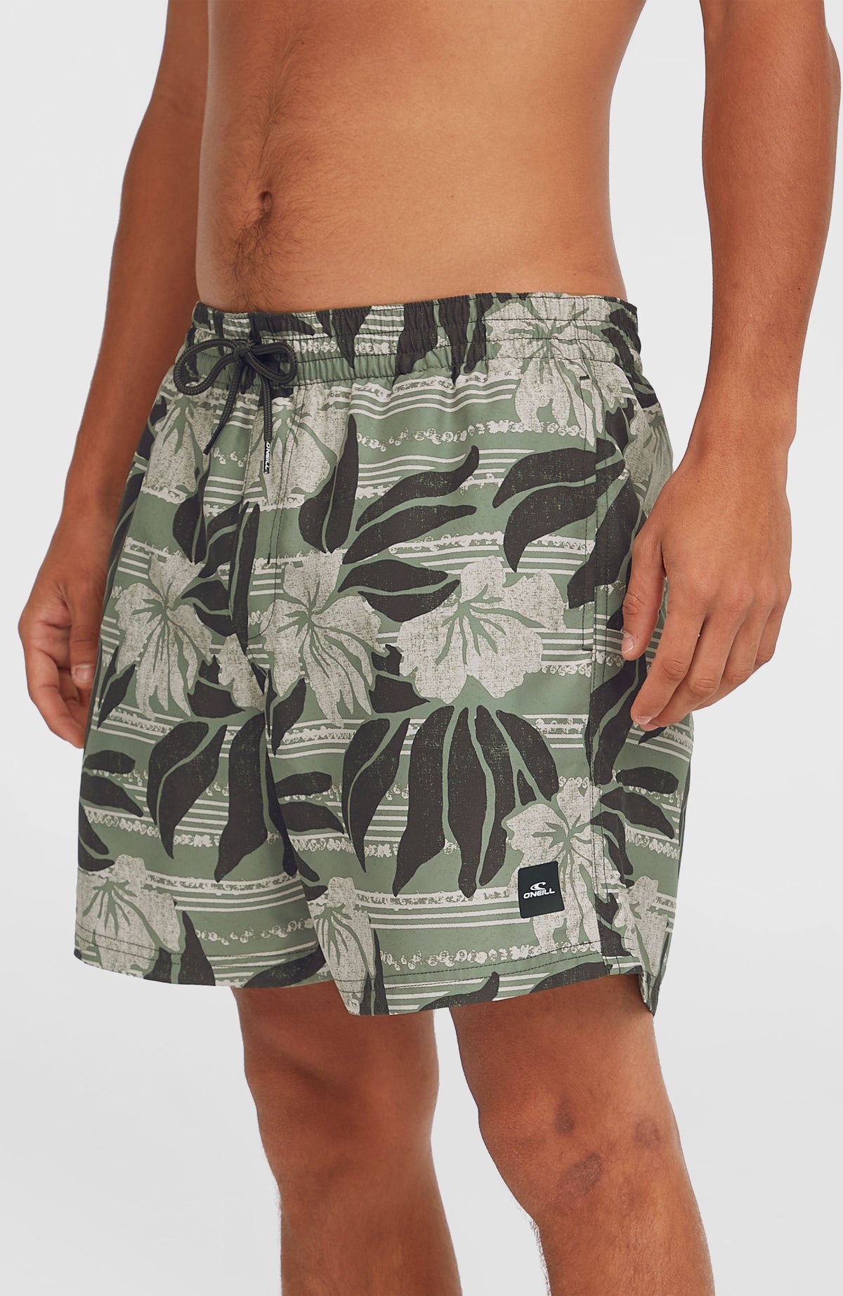 Cali Floral 16'' Badehose für Herren, grün mit Blumenmuster in Weiß und Schwarz, Nahansicht am Model, Logo-Patch am Saum