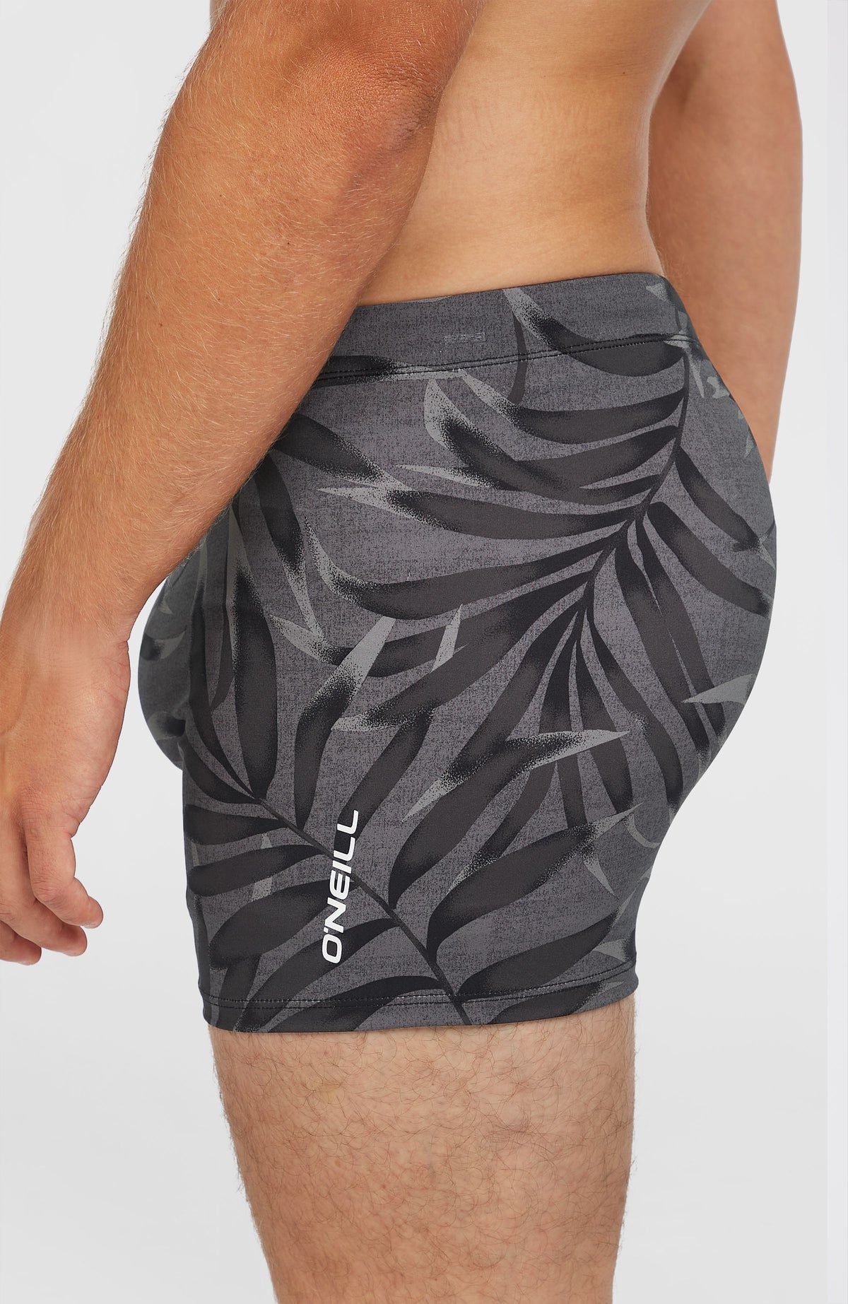 Essentials Floral Racer Badehose, schwarz mit Blättermuster in Grau, Seitenansicht am Model mit Logo-Print