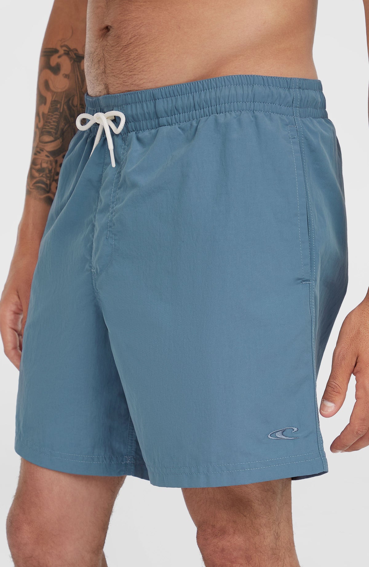 Vert 16'' Badehose für Herren, blau, Nahaufnahme am Model mit Logo-Stickerei am Saum