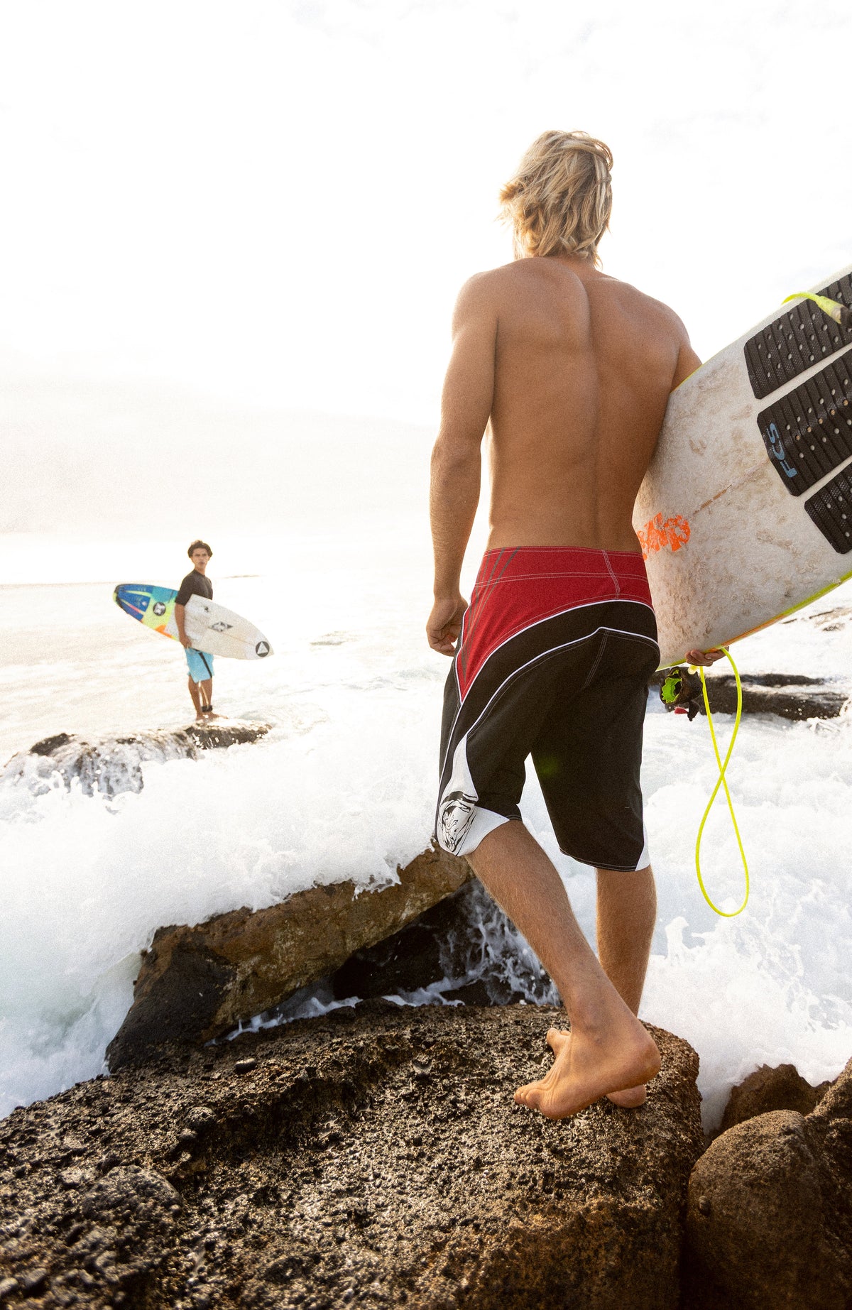 Superfreak Re-Issue Boardshorts für Herren, schwarz, getragen am Model am felsigen Ufer mit Brandung