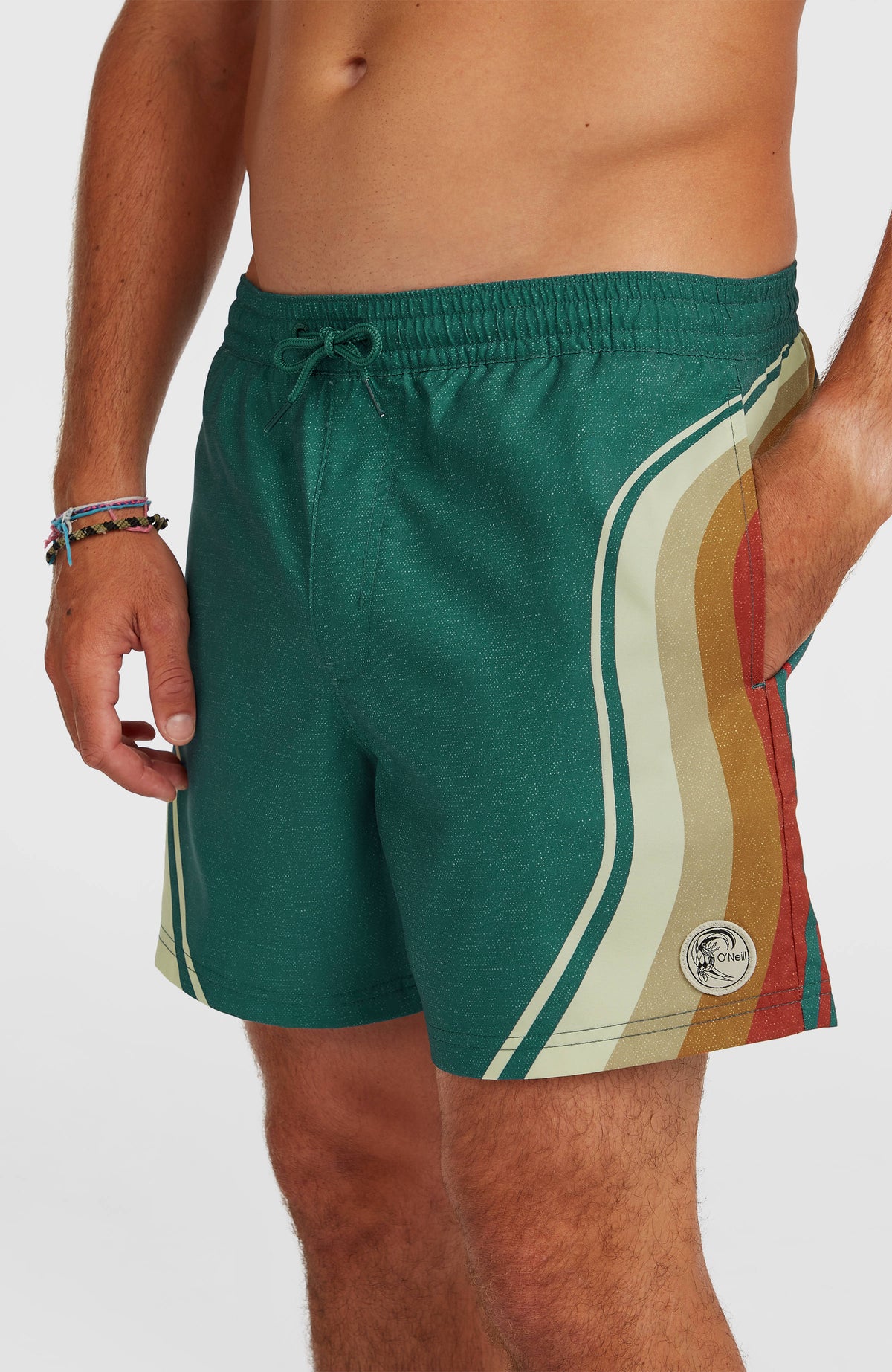 Nahaufnahme der grünen O'Riginals Longboard 15'' Badehose mit Streifenmuster in Beige und Orange, Kordelzug und Logo-Patch