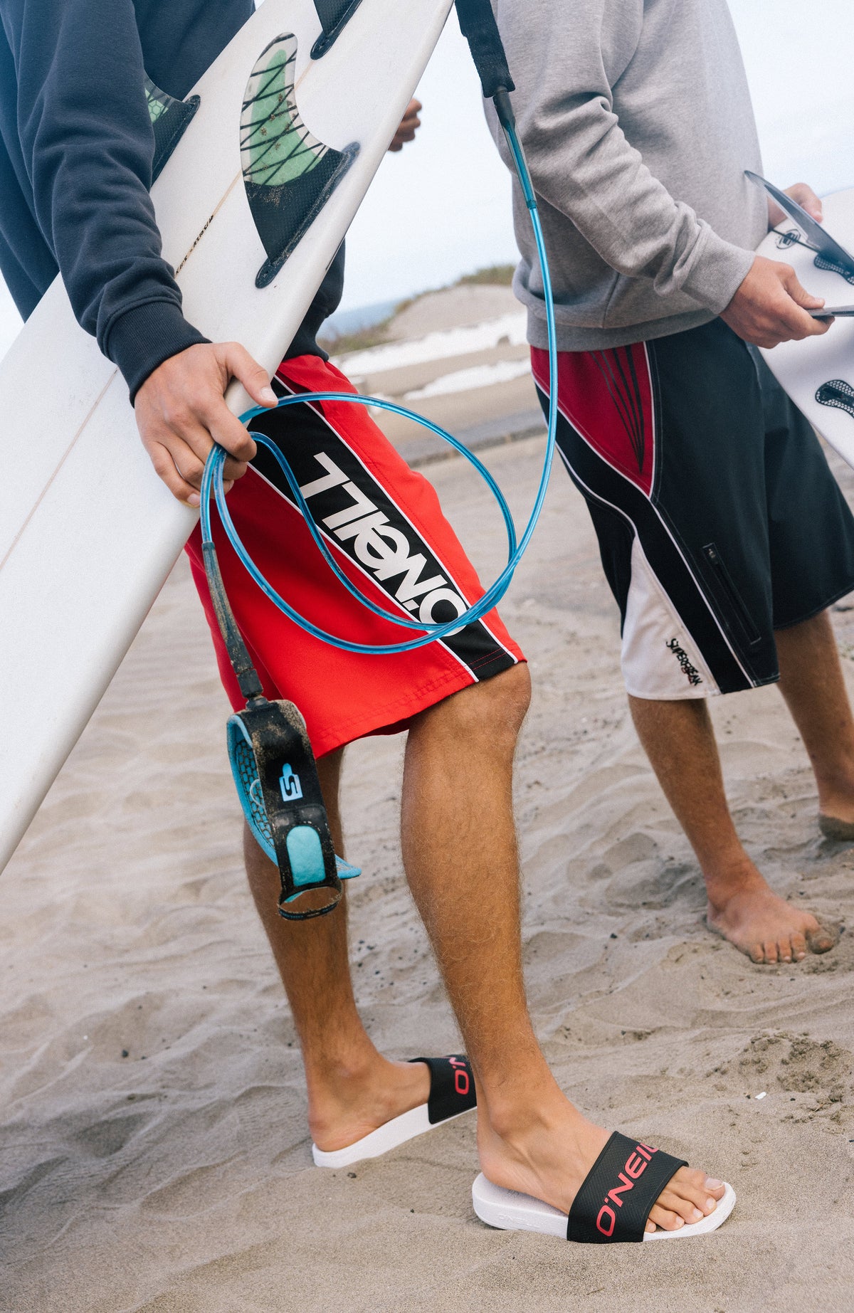 Rote 90s 21'' Badehose mit Logo-Print in Schwarz und Weiß, getragen am Strand mit Surfbrett