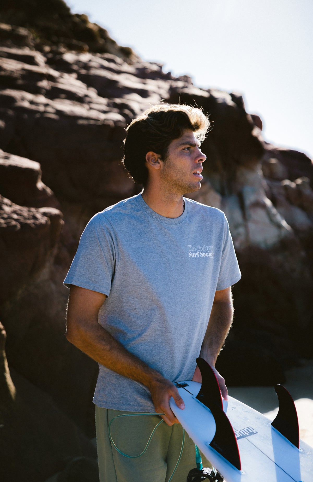 Future Surf Society T-Shirt für Herren, grau mit Logo-Print in Weiß, getragen am Model vor Felsen