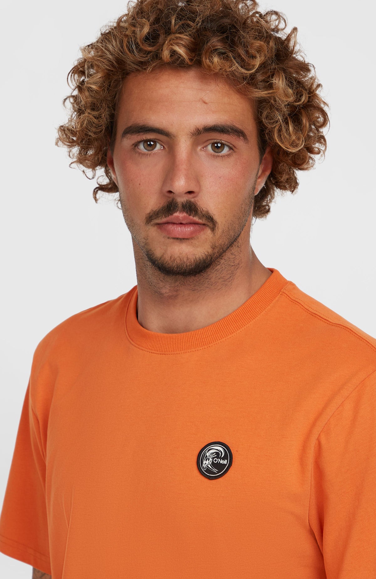 O'Riginals Badge T-Shirt für Herren, orange, Nahaufnahme am Model mit Fokus auf das runde Logo-Badge